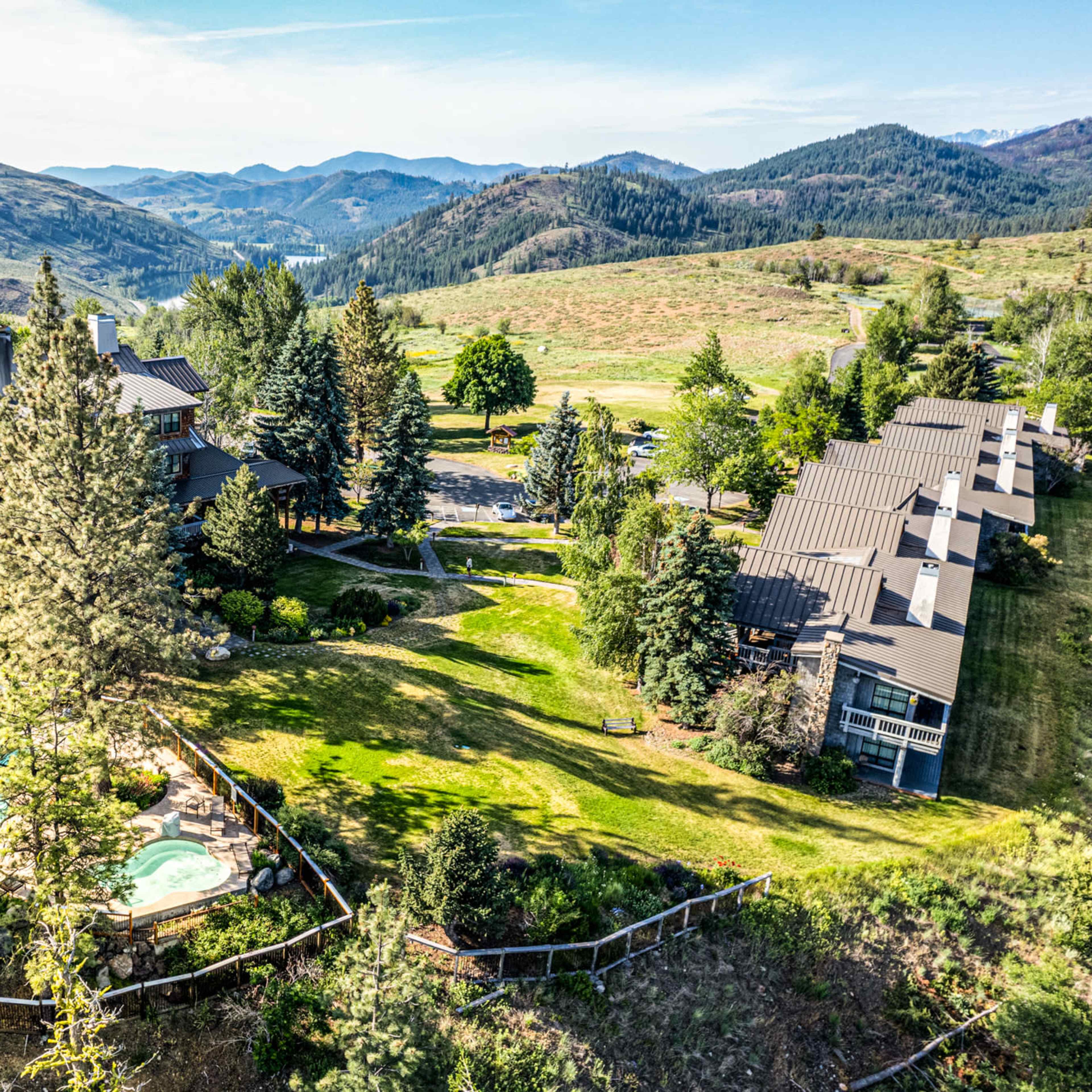Aerial view of a large lodge with a swimming pool surrounded by trees and mountains in the background.