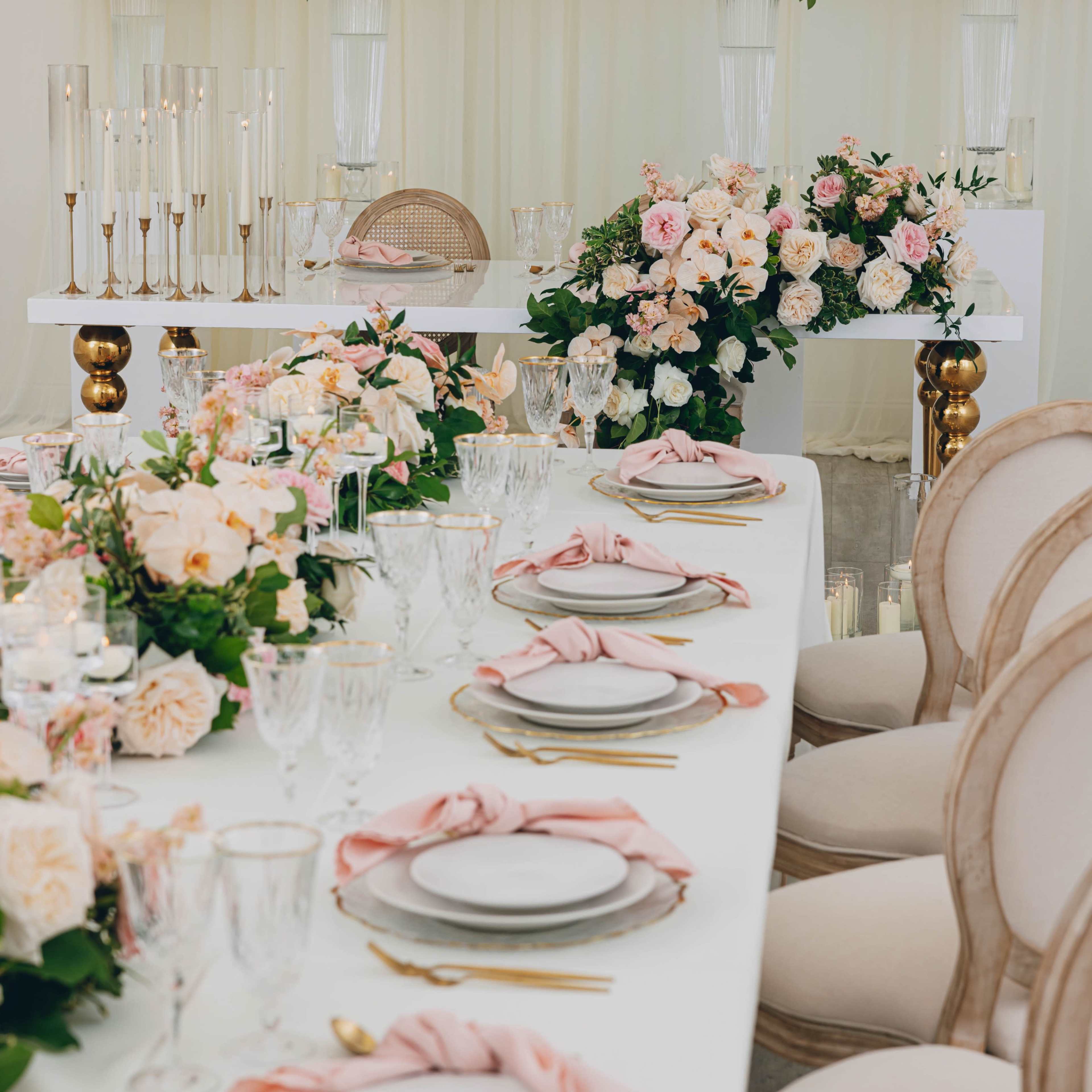 A elegantly set dining table adorned with floral arrangements and decorative tableware in a spacious, well-lit venue.