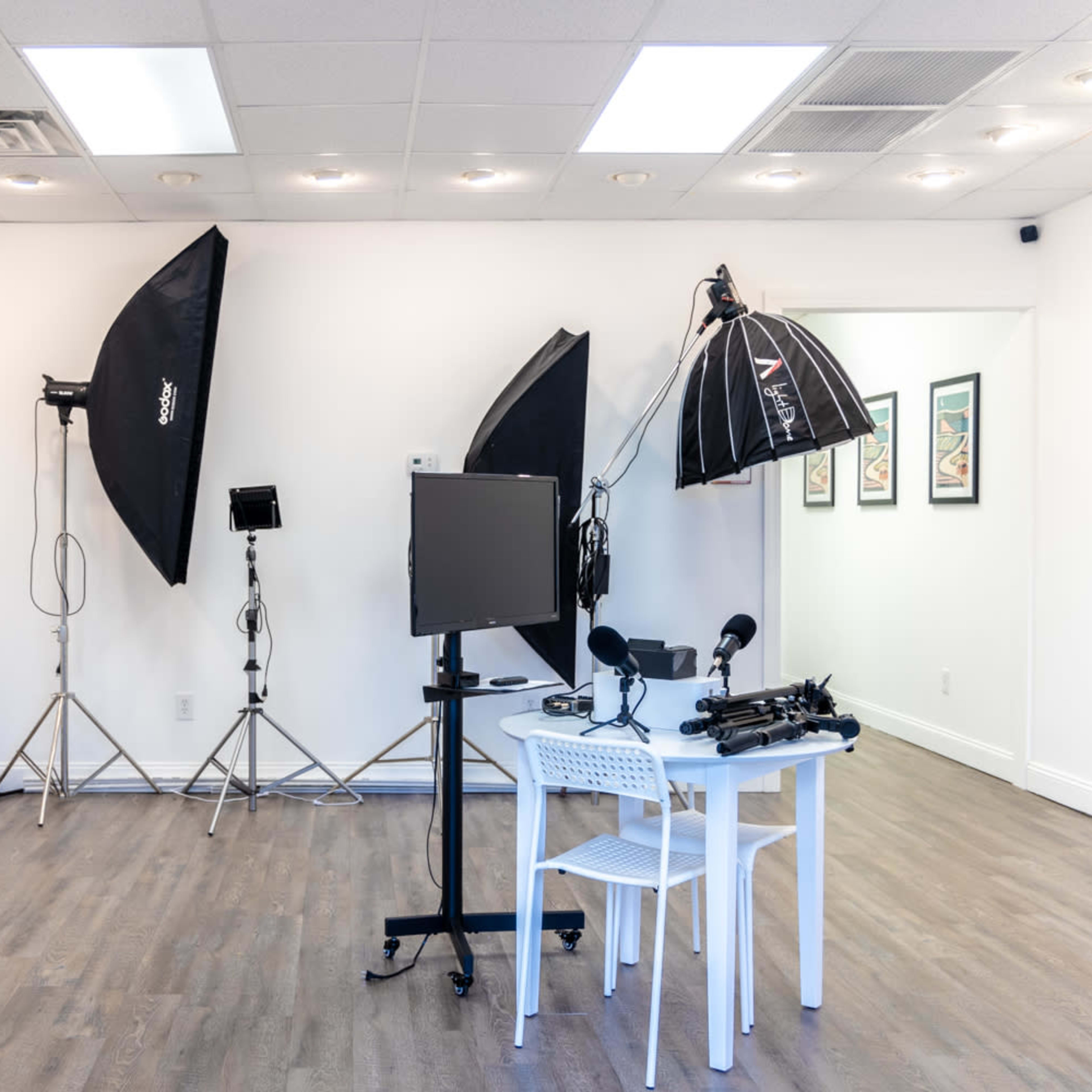 A bright, empty photography studio contains lighting equipment, a monitor, and a small table with microphones.