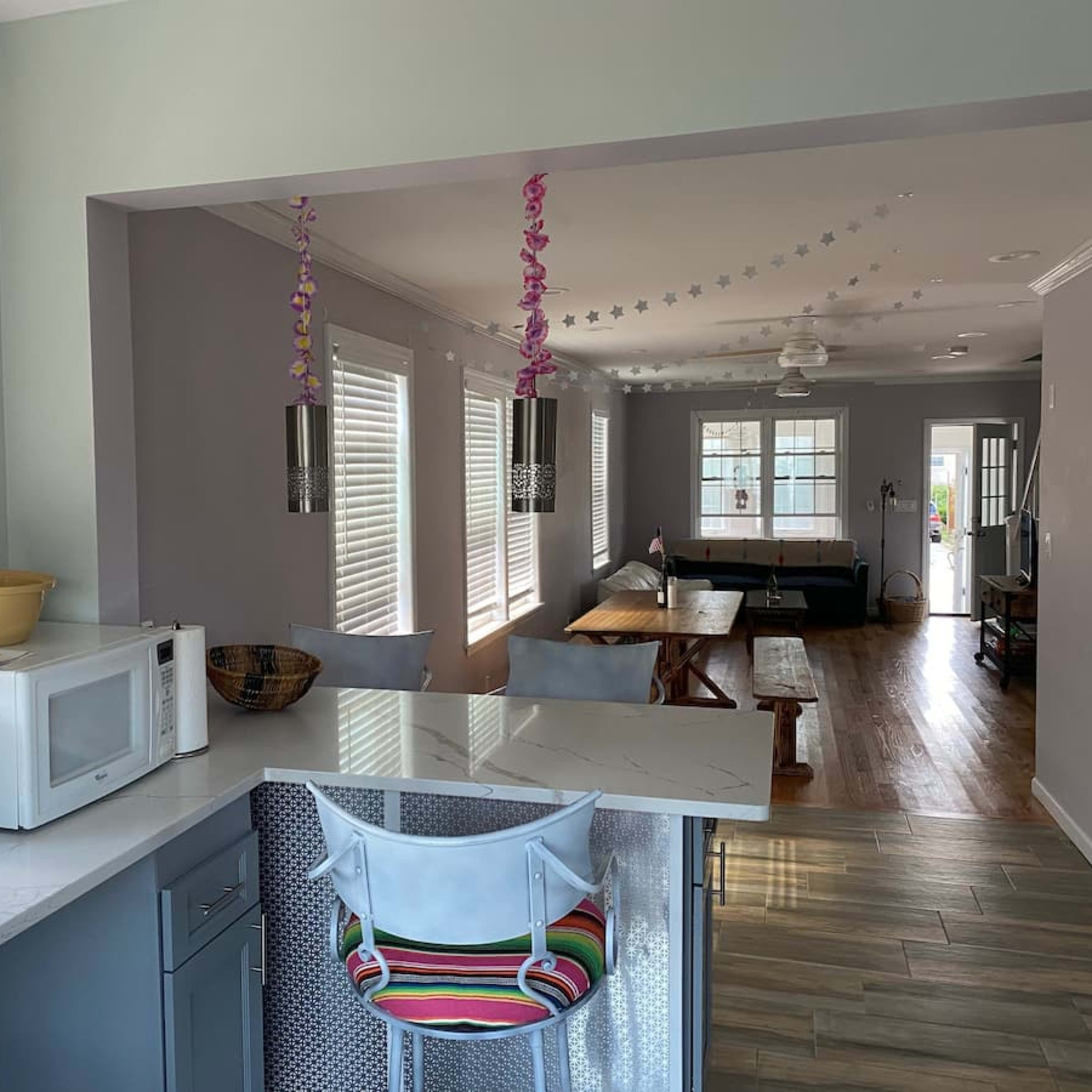 A modern kitchen area with a microwave, a bowl of fruit, and a barstool, leading into a living room with a table and couch.