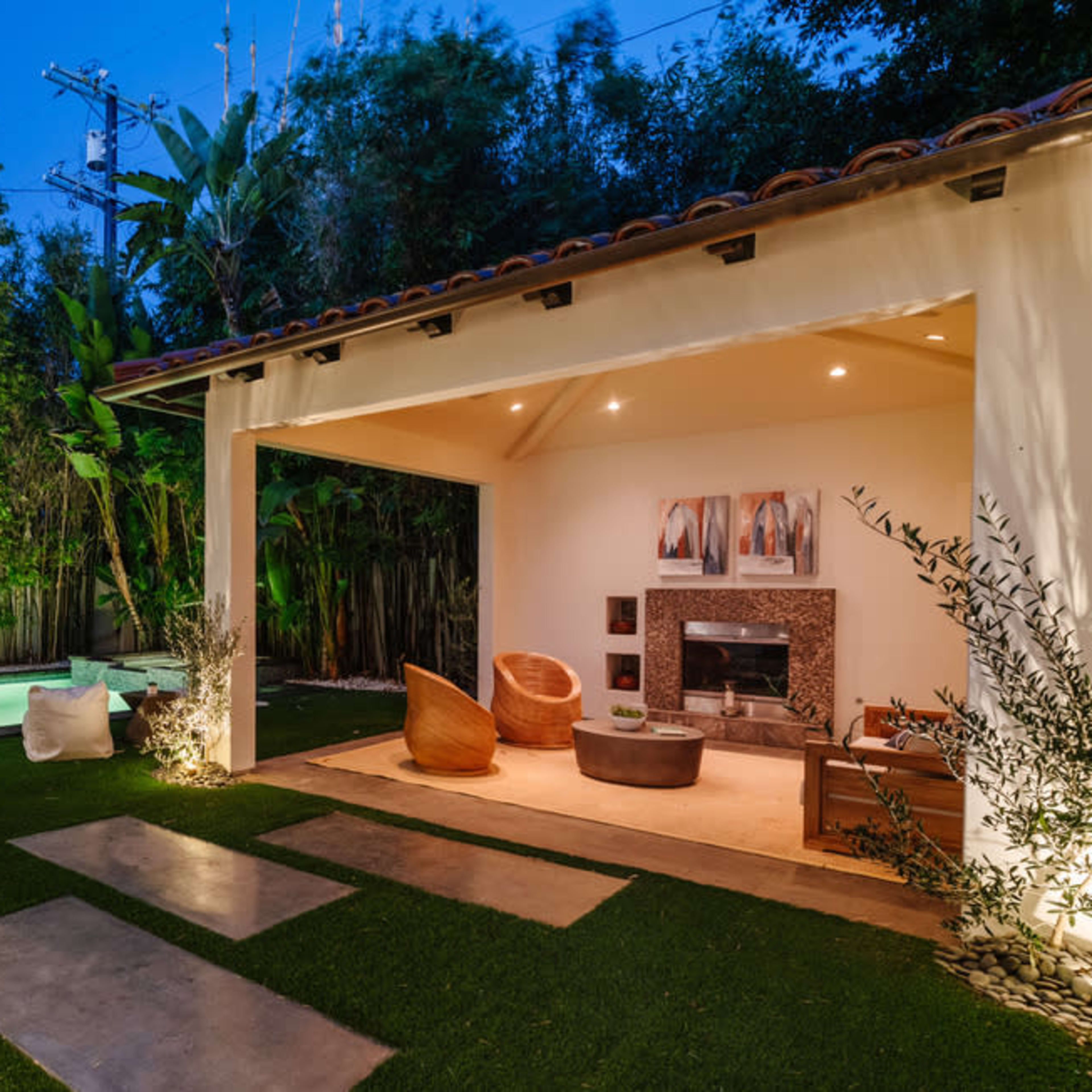 A modern outdoor space featuring a small swimming pool, manicured grass, a seating area with stylish furniture, and surrounding greenery.