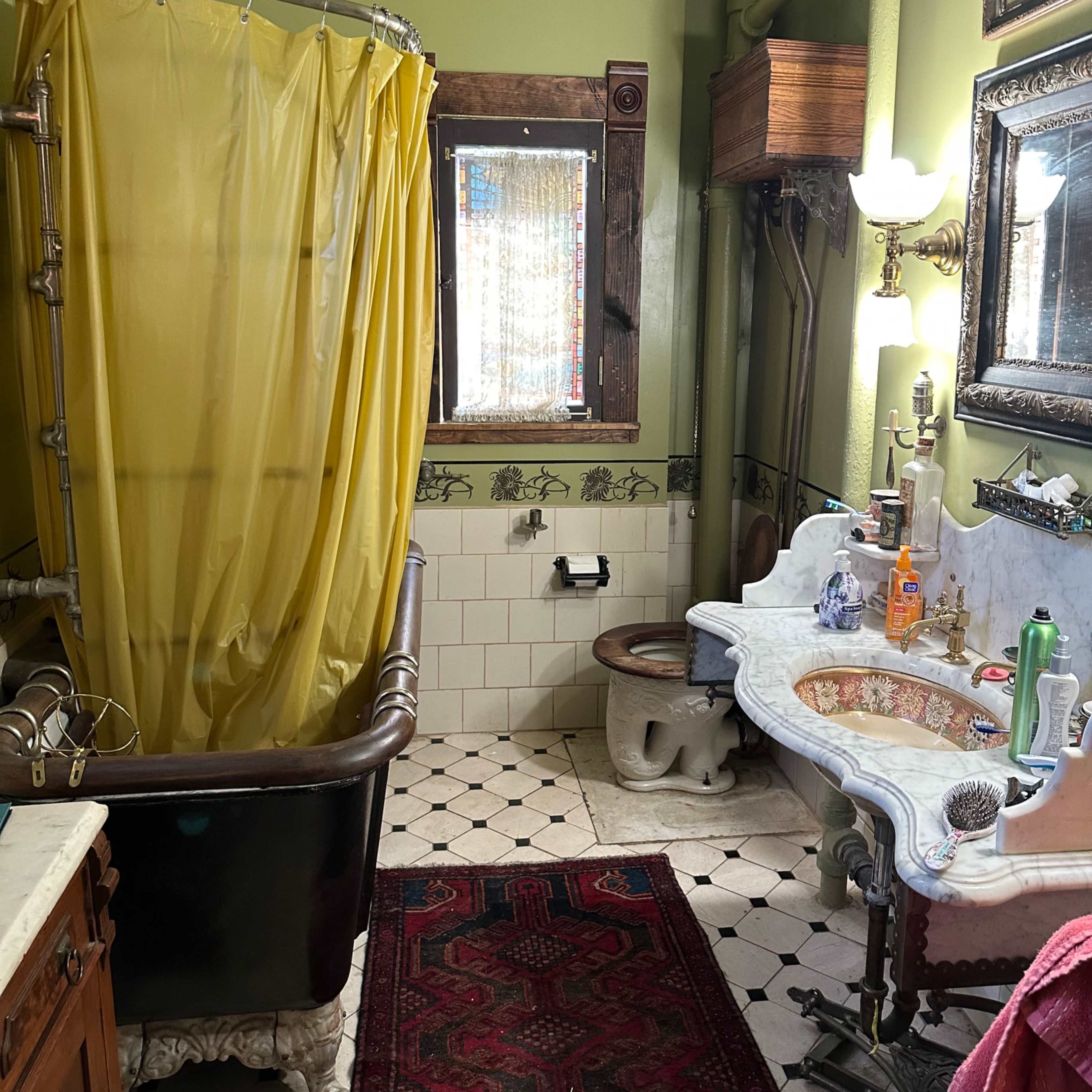 A vintage bathroom featuring a clawfoot bathtub with a yellow shower curtain, a decorative sink with an ornate mirror, and patterned tile flooring.