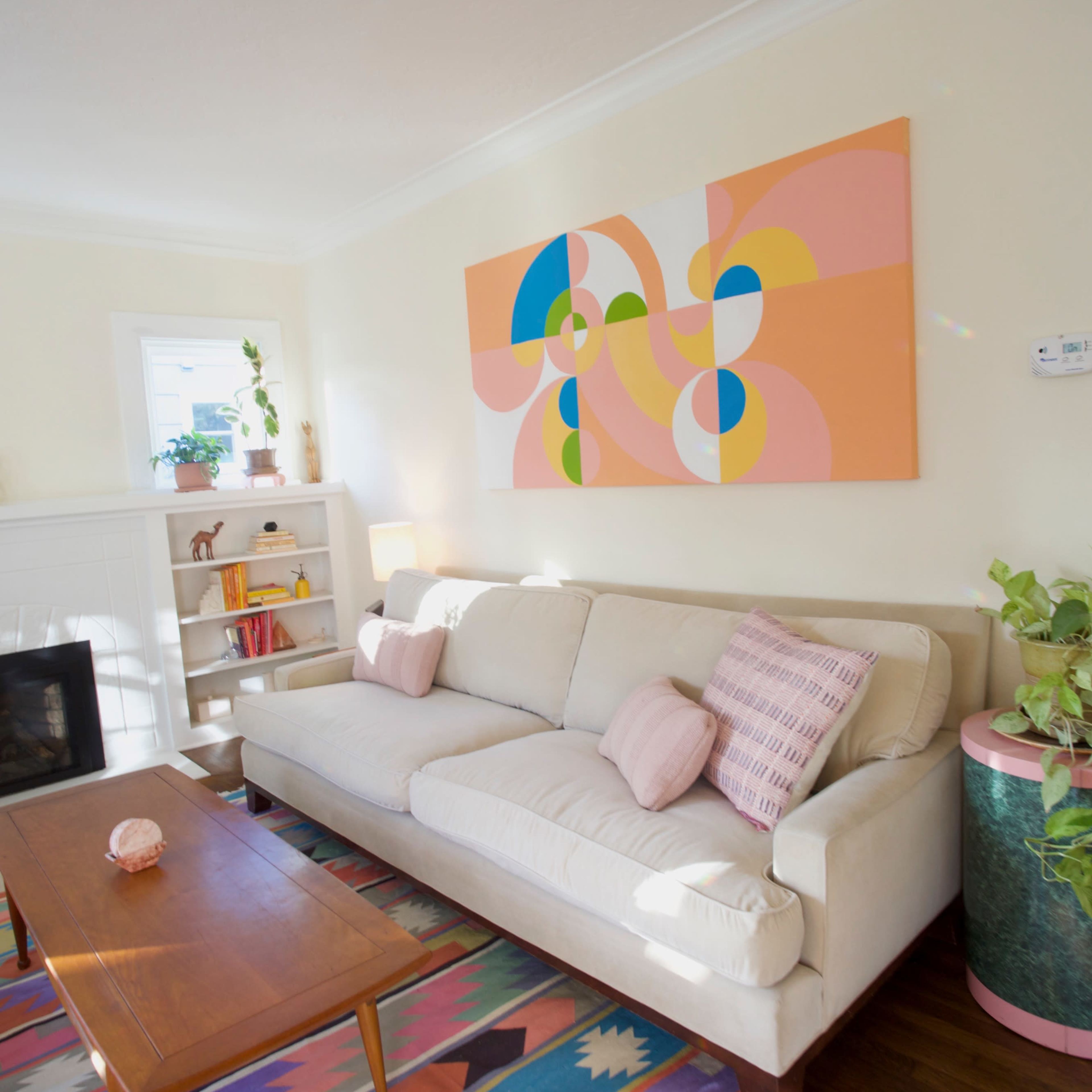 A bright living room with a light-colored sofa, a wooden coffee table, and a colorful area rug, featuring a large abstract artwork on the wall.