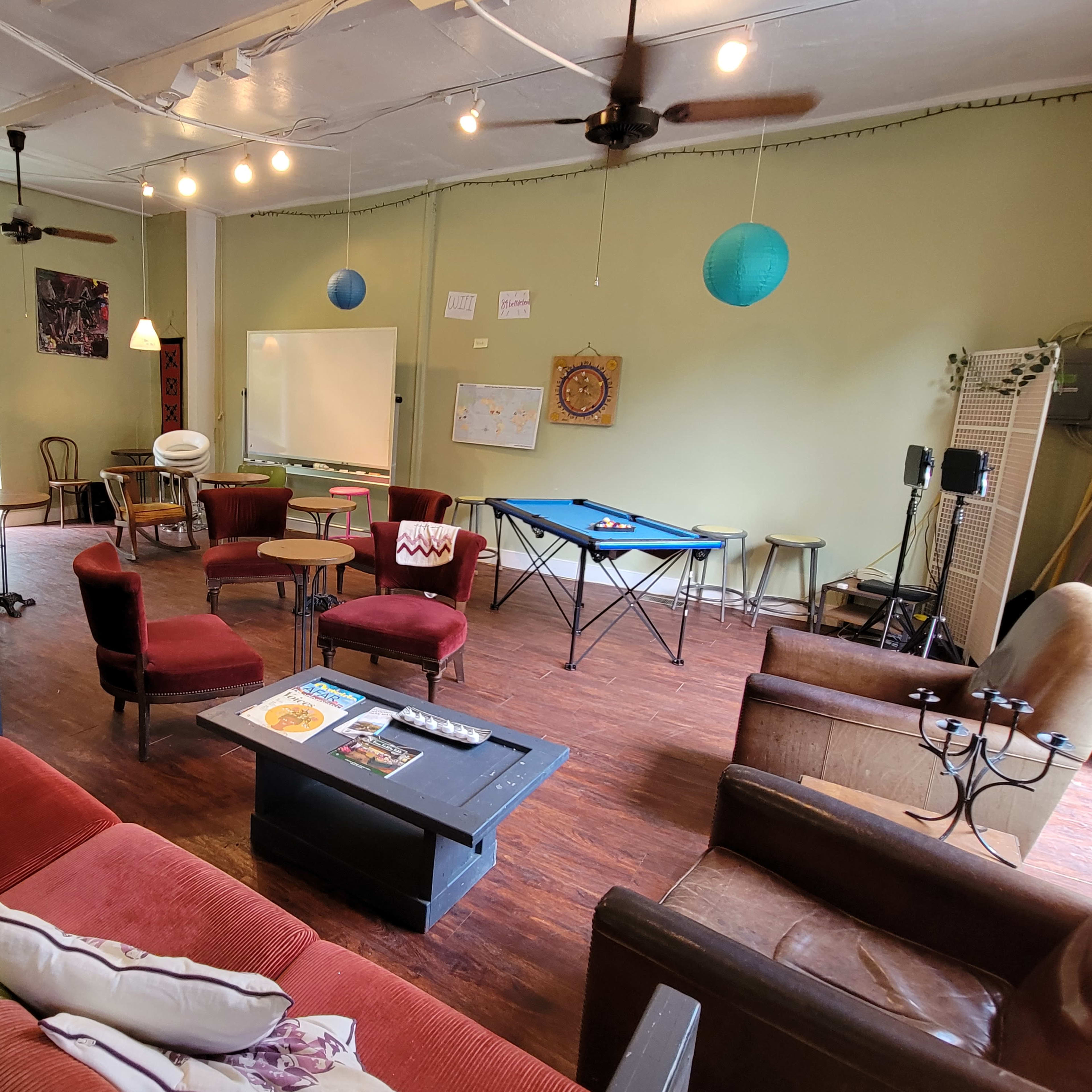 A cozy multi-purpose room furnished with seating, a table, and decorative elements, featuring green walls and ceiling lights.