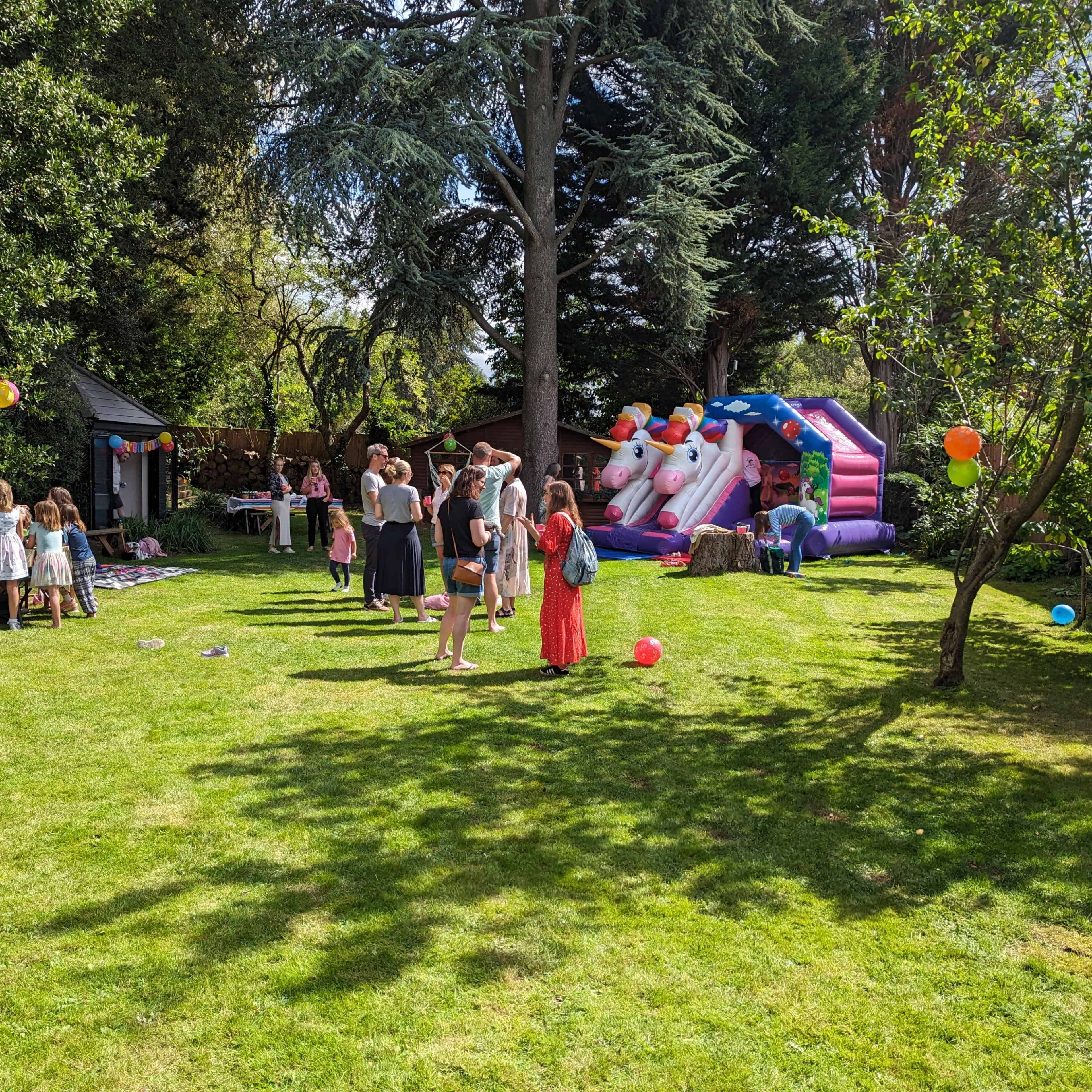 A group of children and adults gather in a backyard with a bounce house and various colorful decorations.