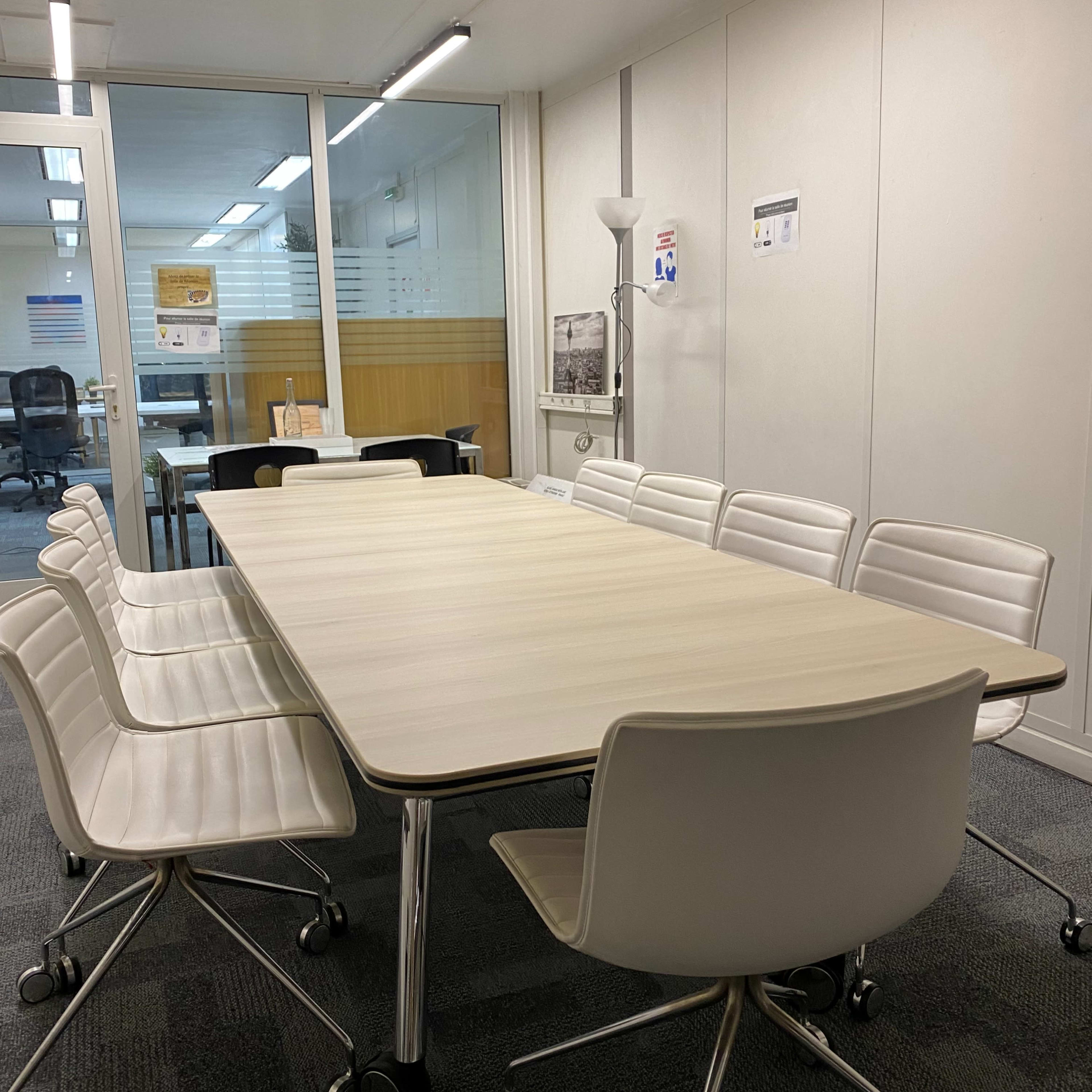 A modern conference room features a long wooden table surrounded by white rolling chairs.