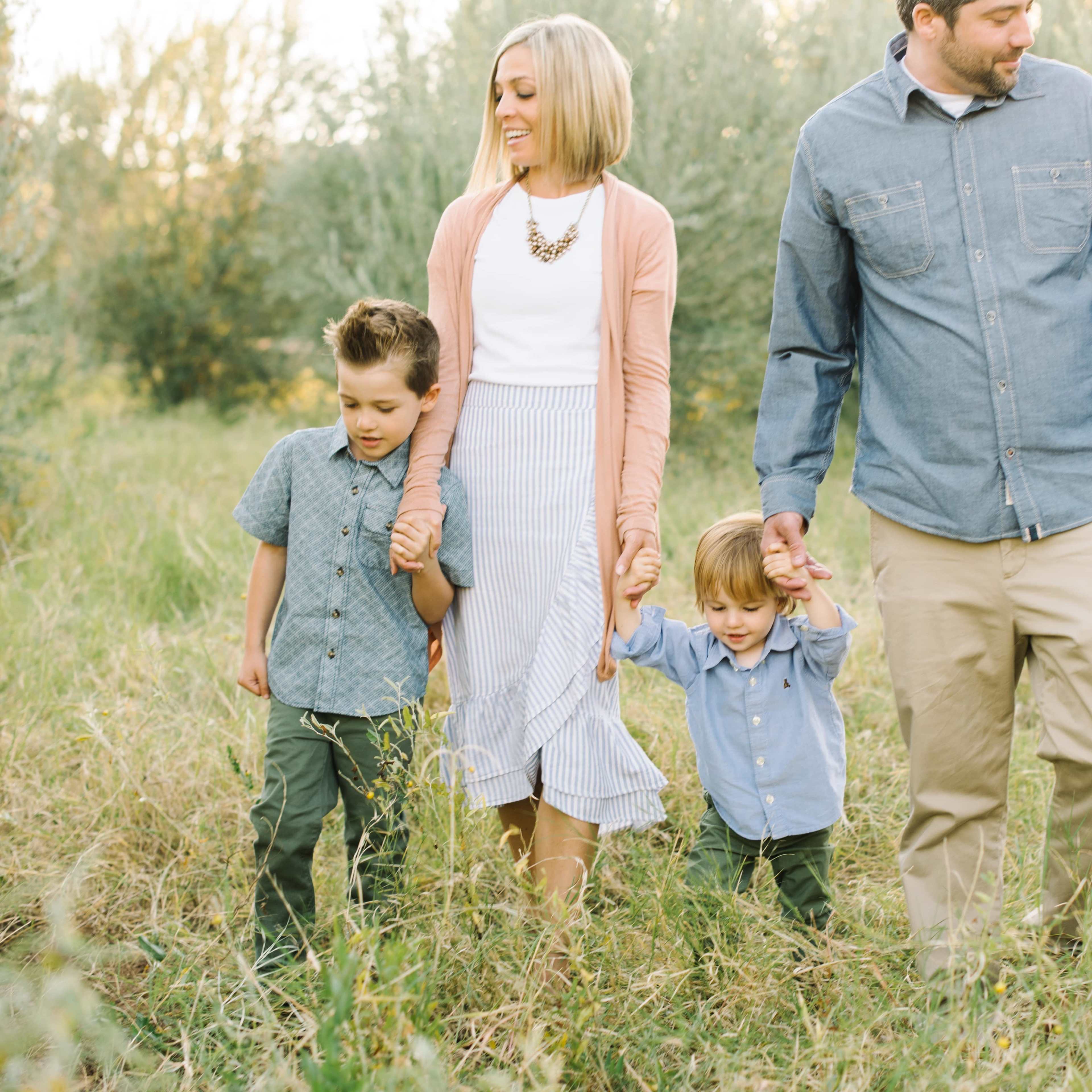A family of five walks hand-in-hand through a grassy area with trees in the background.