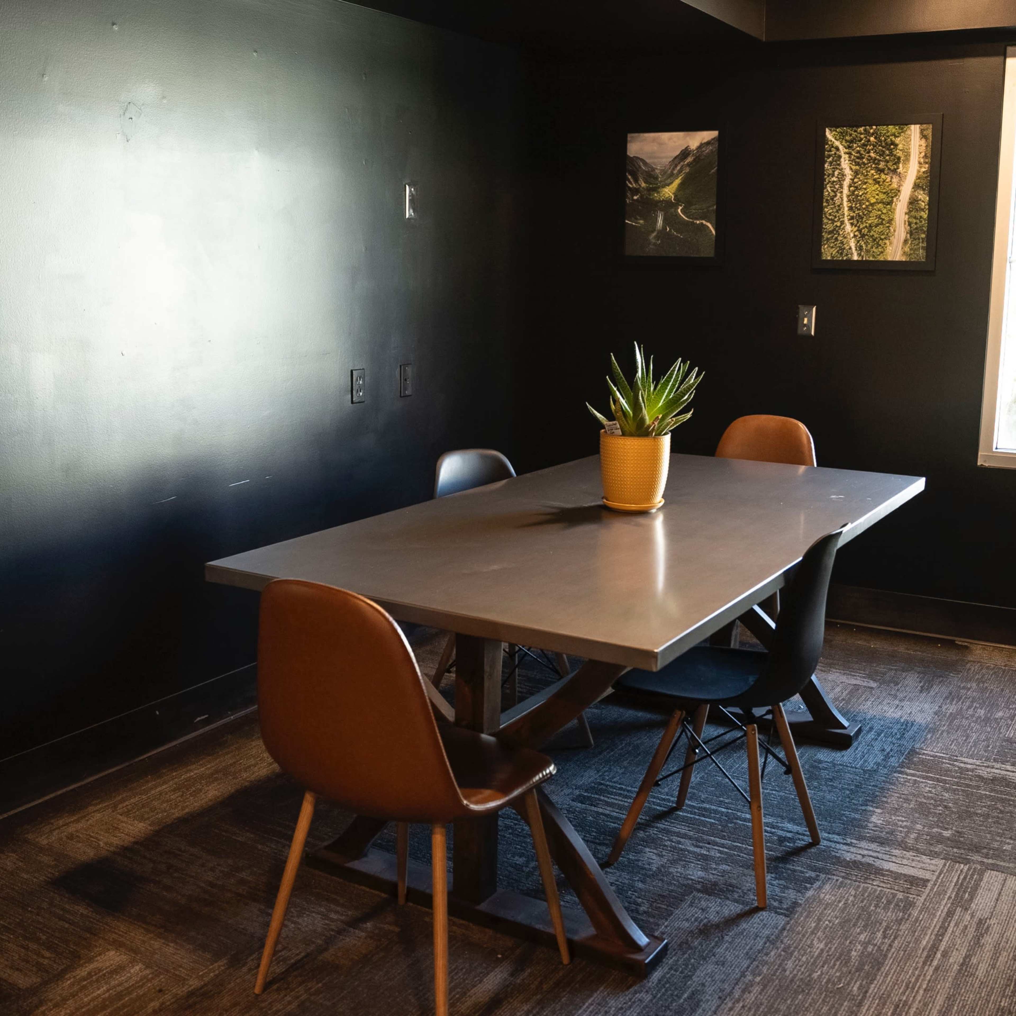 A small conference room with a table and four chairs, a potted plant in the center, and two framed pictures on the wall.