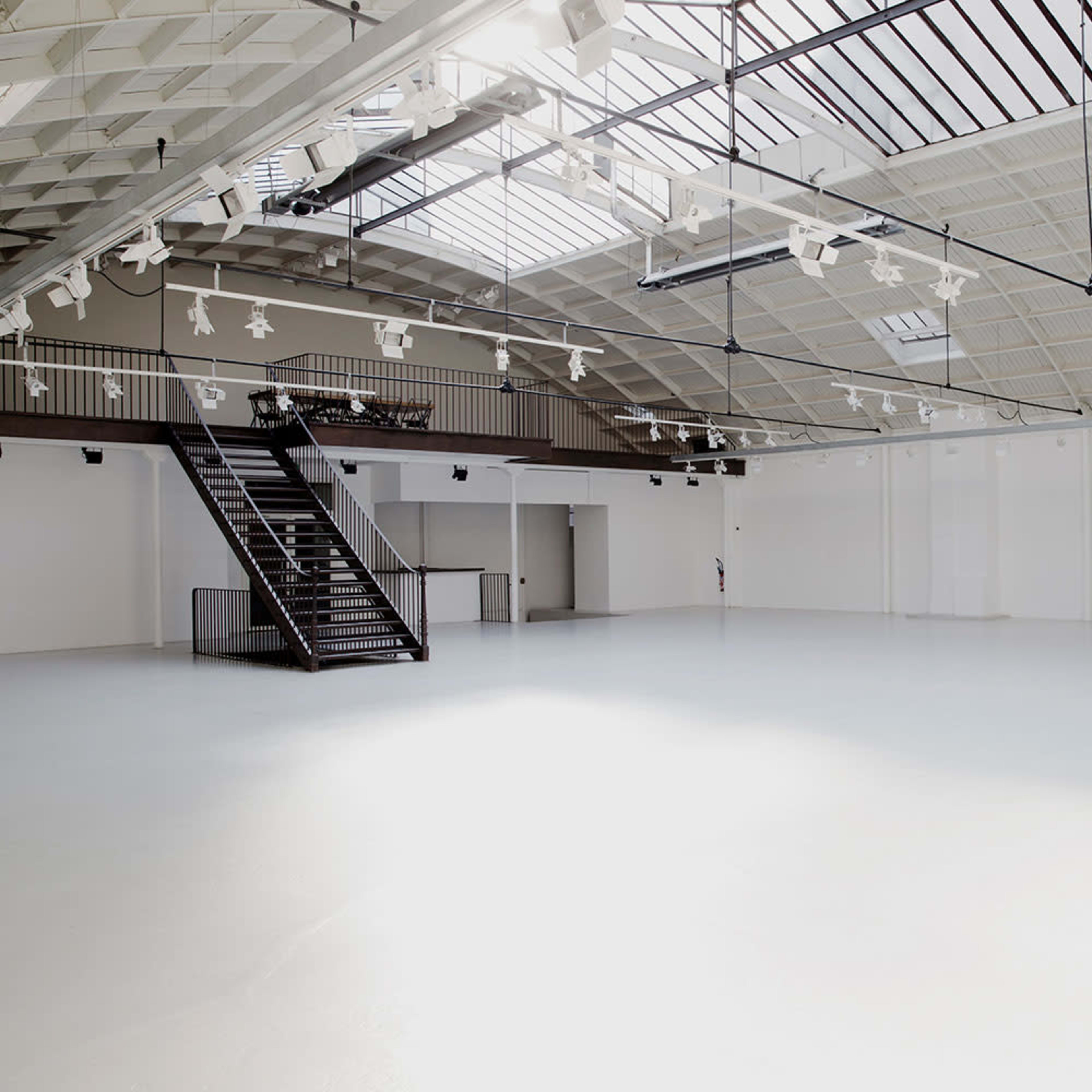 A spacious, empty room with a high ceiling, large skylights, and a staircase on one side.
