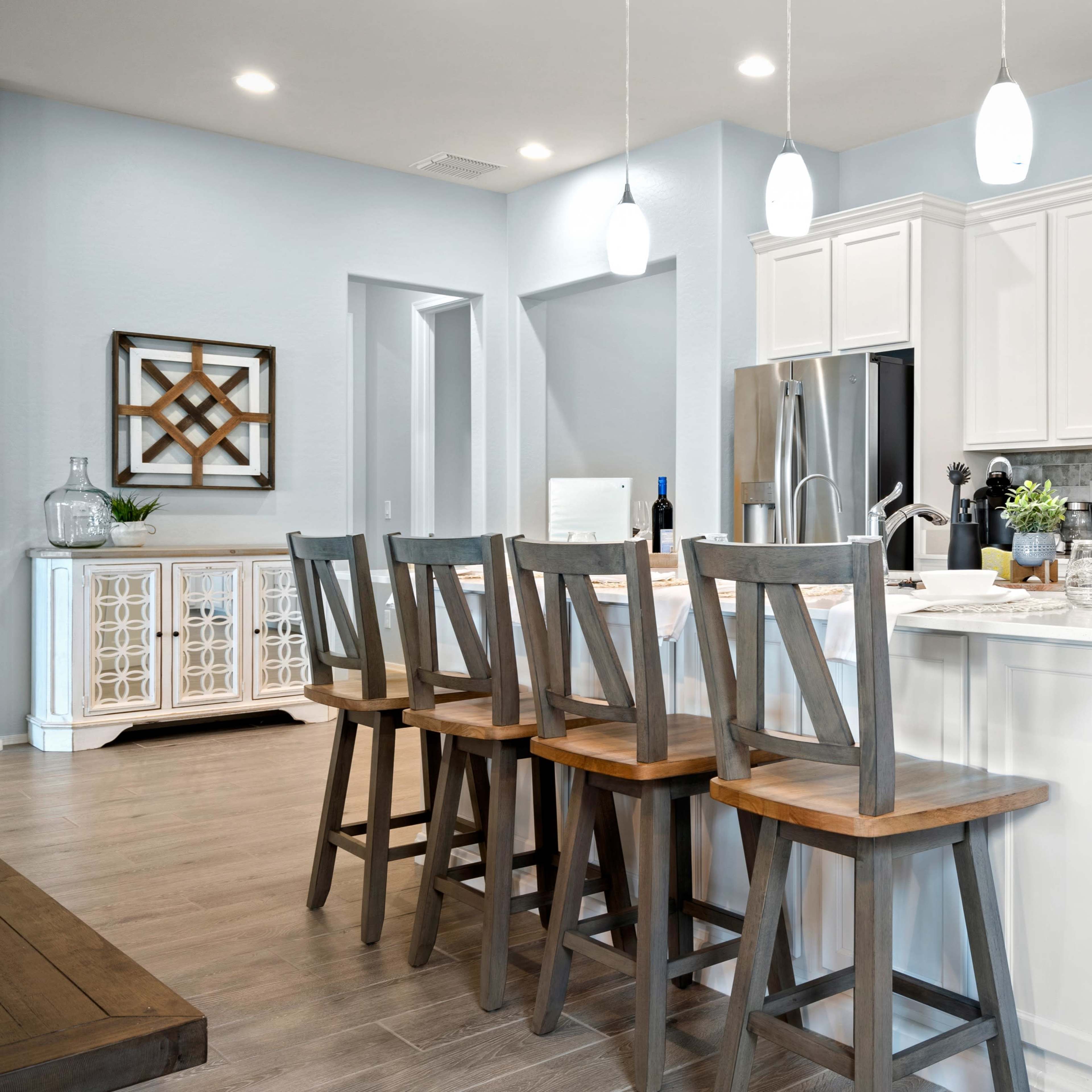 A modern kitchen features white cabinetry, stainless steel appliances, and a large island with wooden stools.