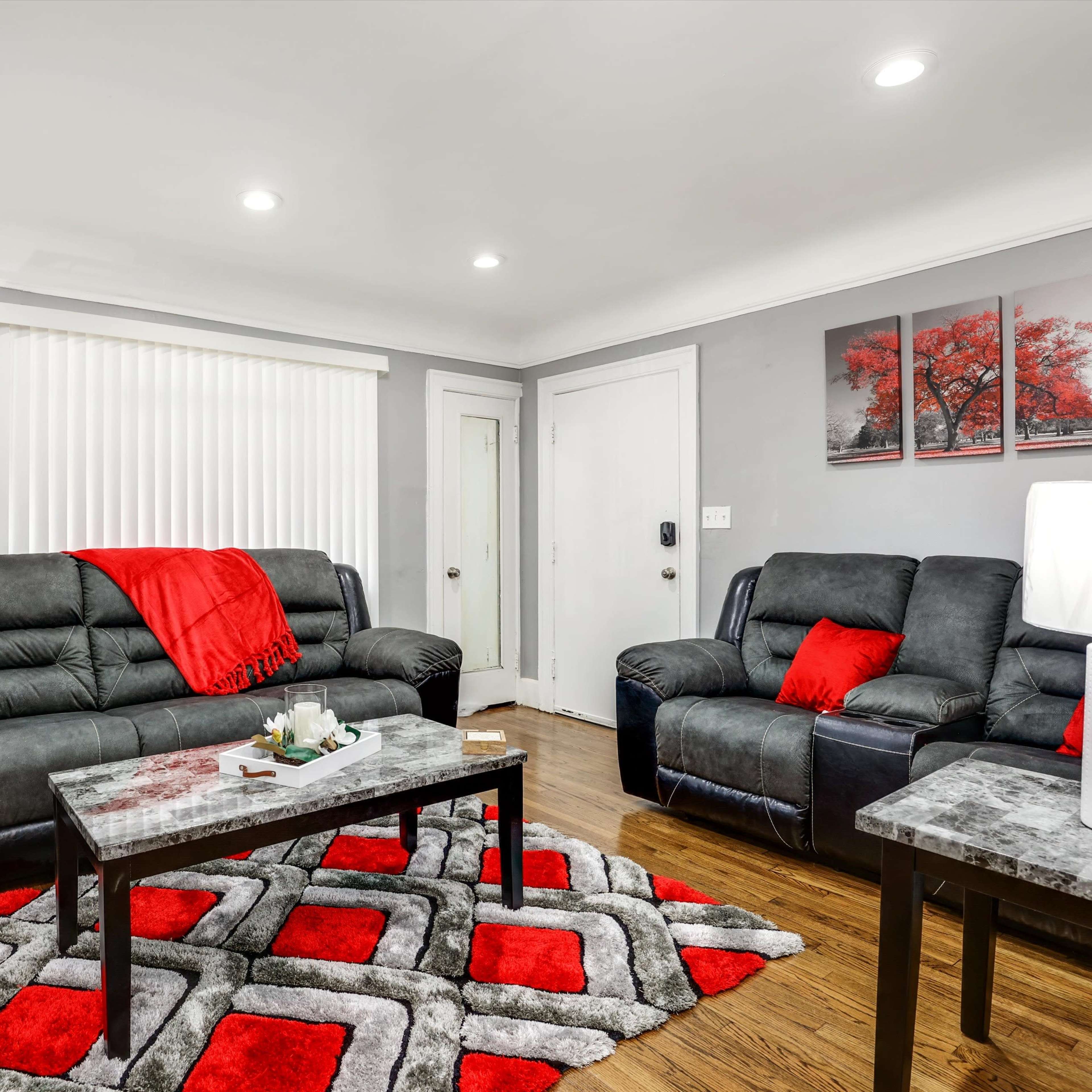 The living room features dark sofas with red accents, a patterned rug, and modern lighting, complemented by artwork on the walls.