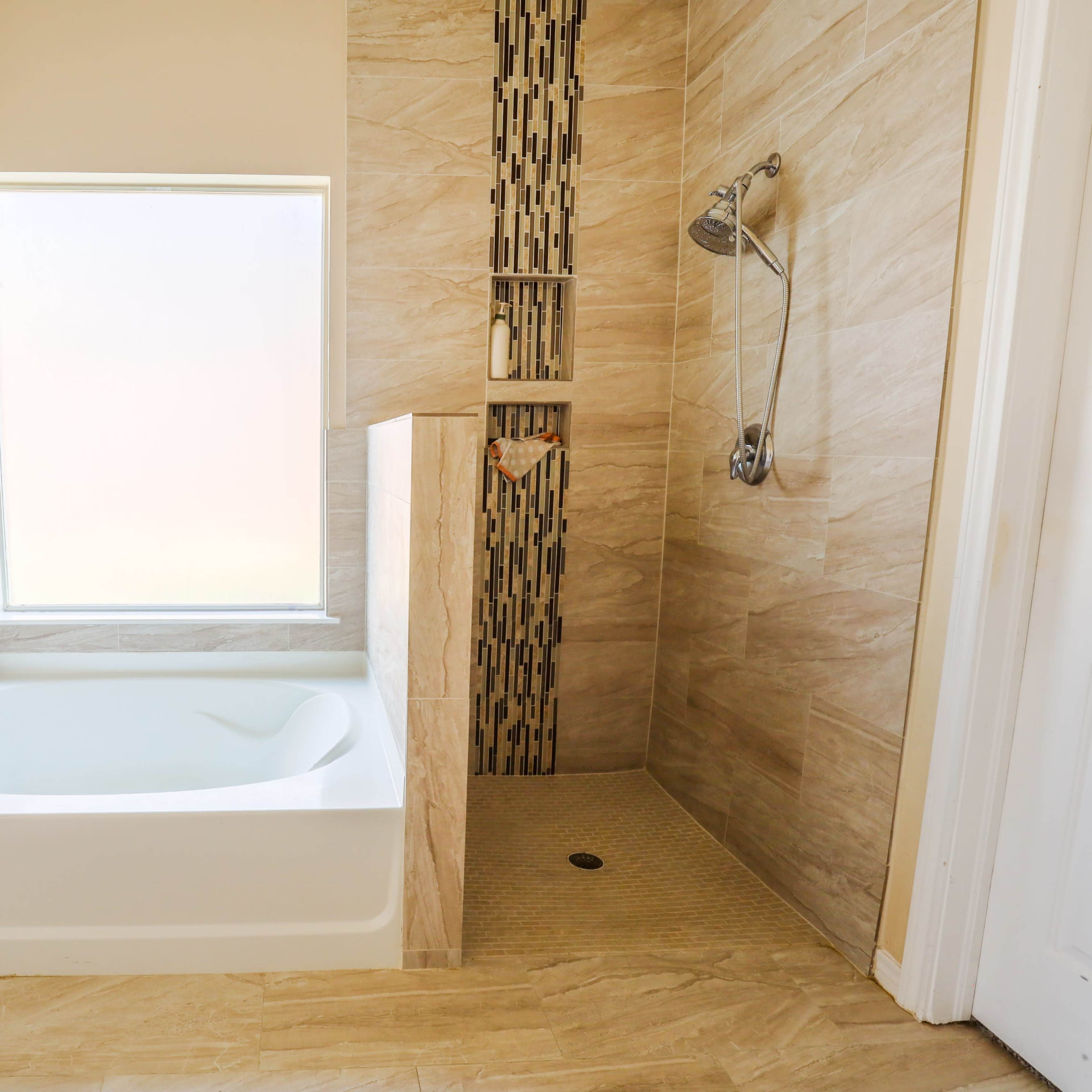 A bathroom featuring a bathtub next to a glass window and a tiled shower area with a built-in shelf.
