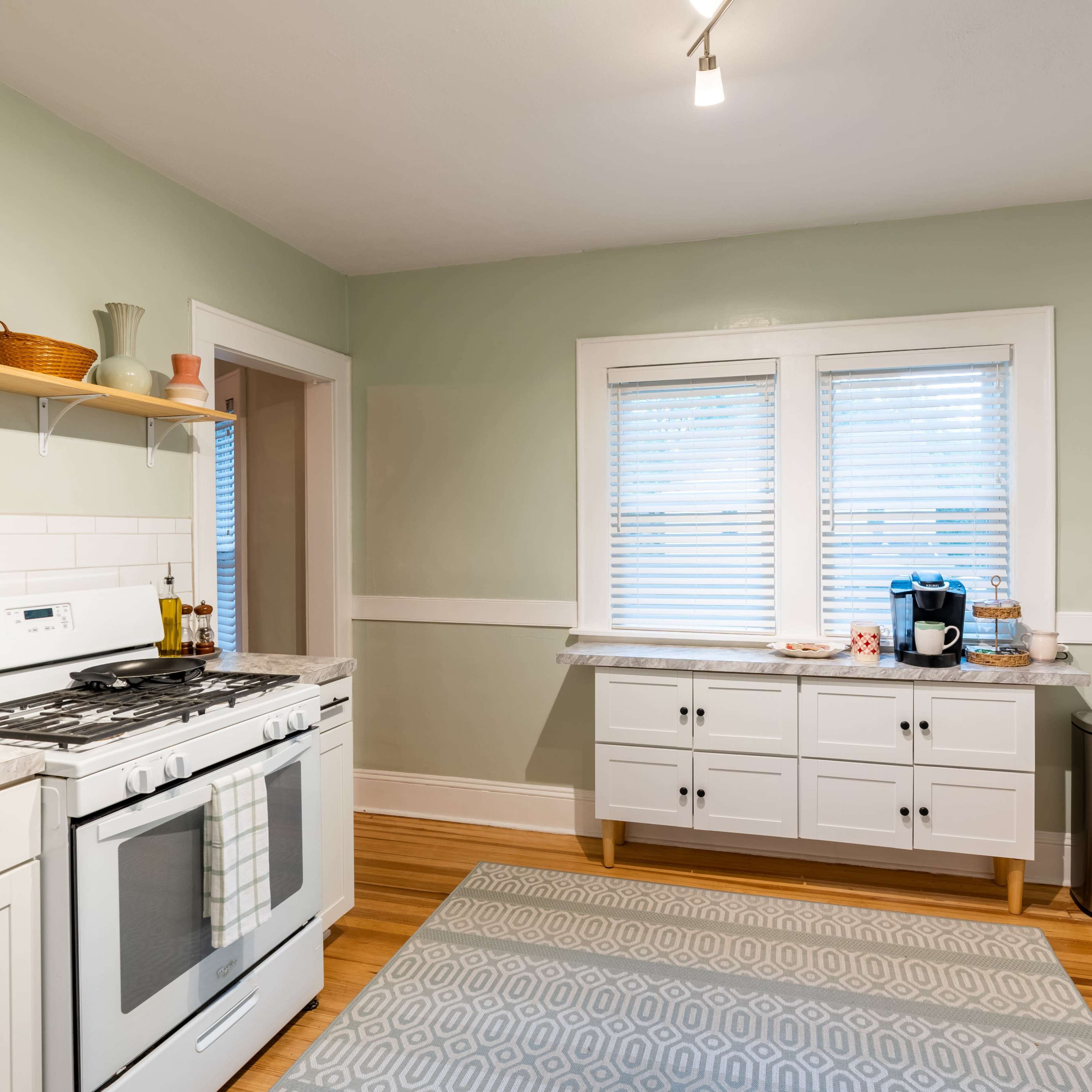A modern kitchen with a gas stove, a light green wall, a countertop with a coffee maker, and wooden flooring.