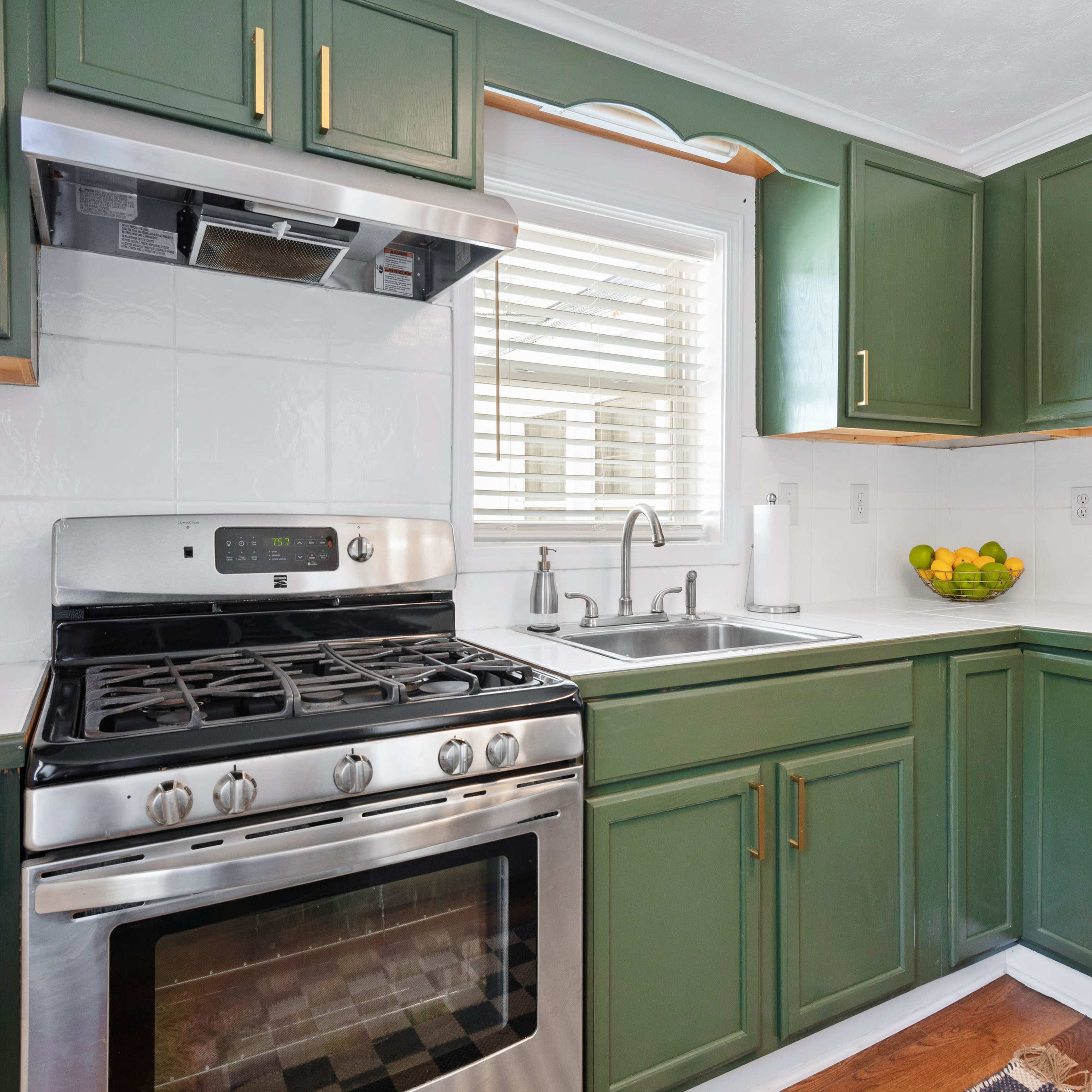 The kitchen features green cabinets, stainless steel appliances, and a double sink beneath a window.