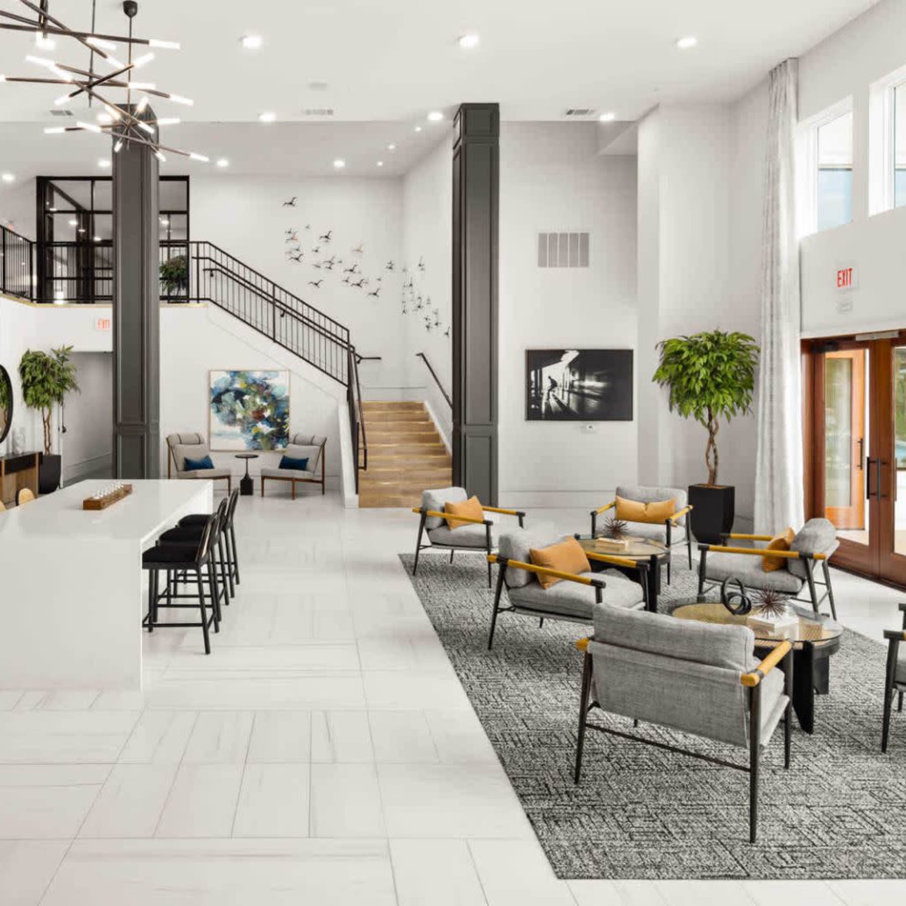 A modern lobby with a seating area, a kitchen counter, and a staircase leading to an upper level.