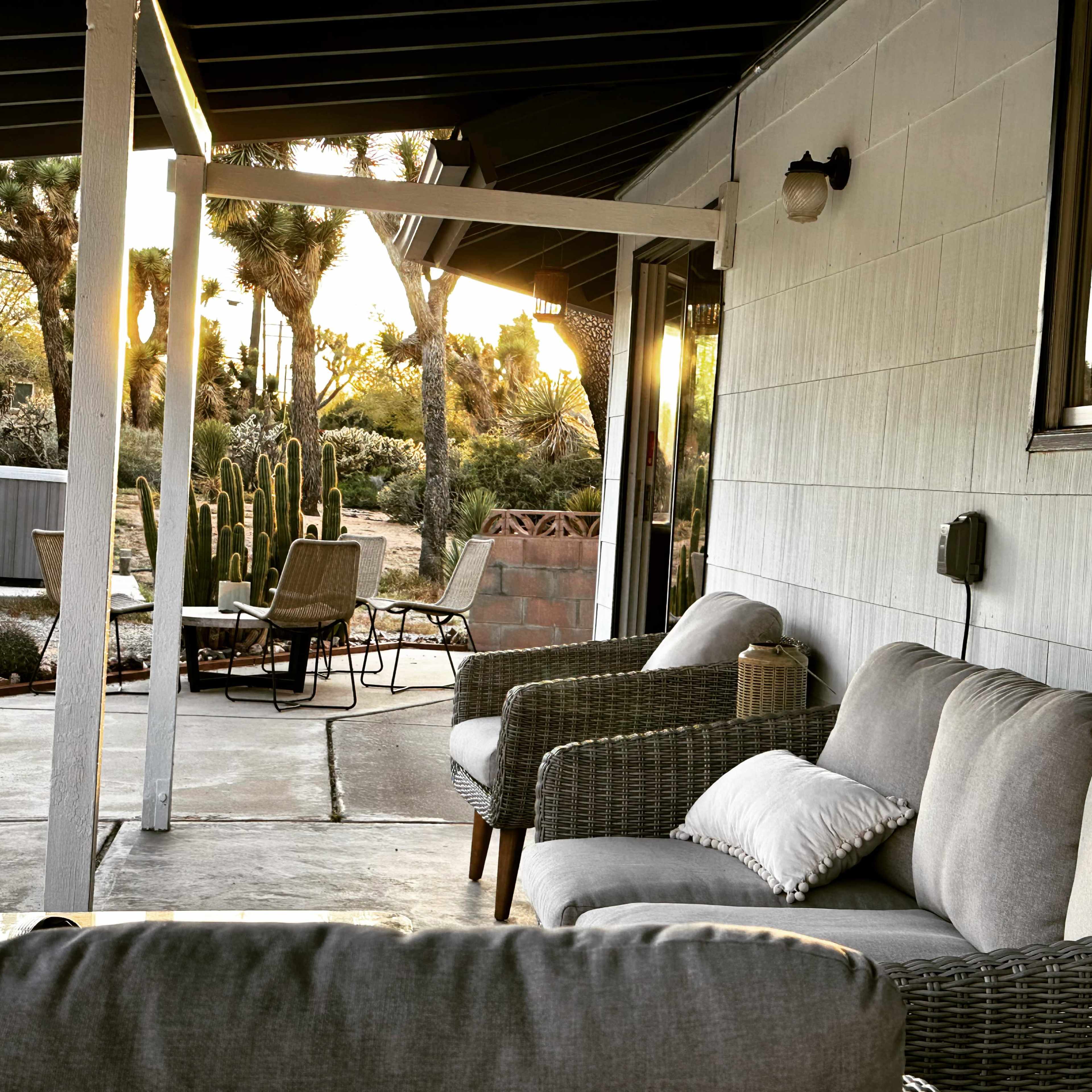 A porch with gray sofas and a lantern overlooks a desert landscape with cacti at sunset.