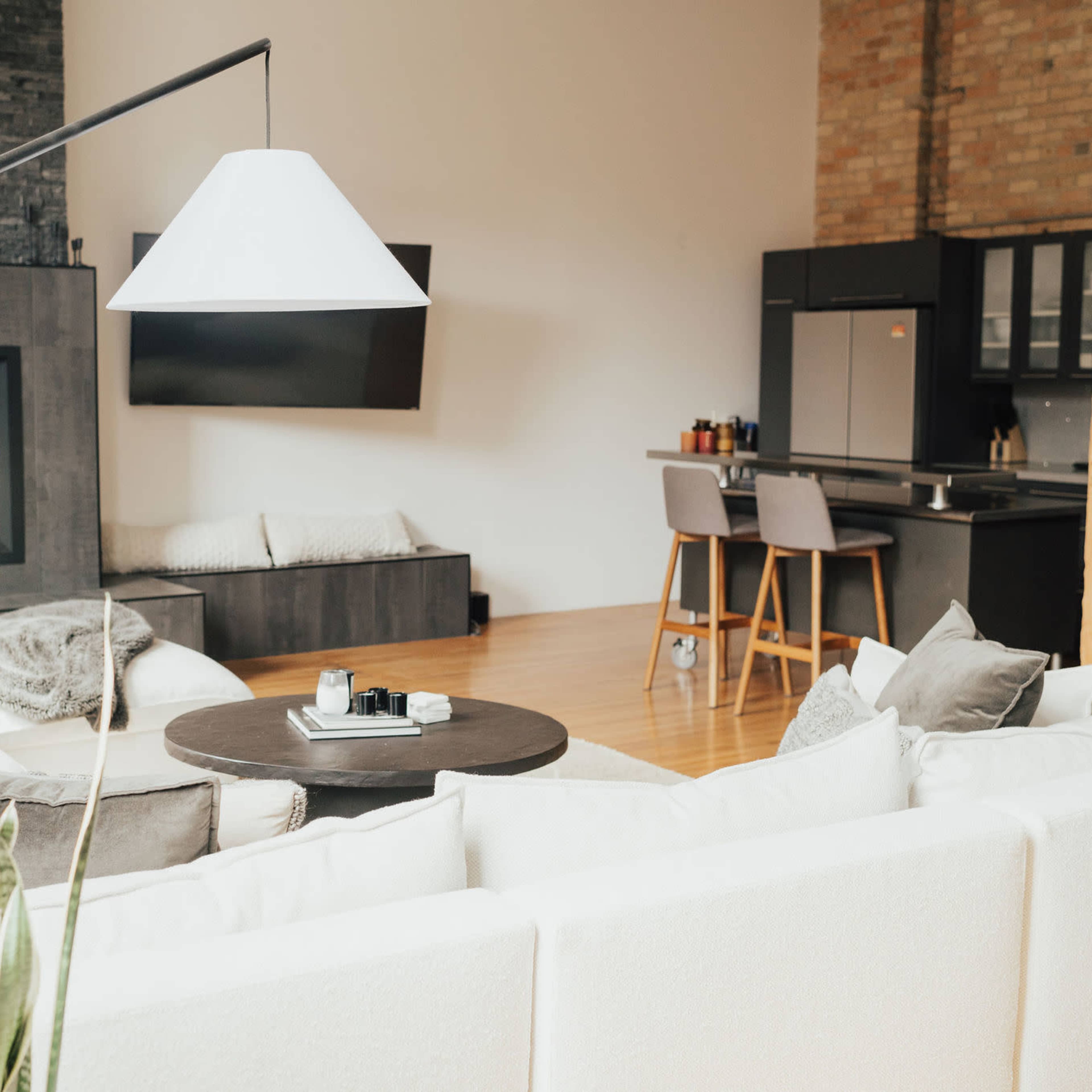 A spacious, modern living room with a large sectional sofa, a round coffee table, and a kitchen area visible in the background.