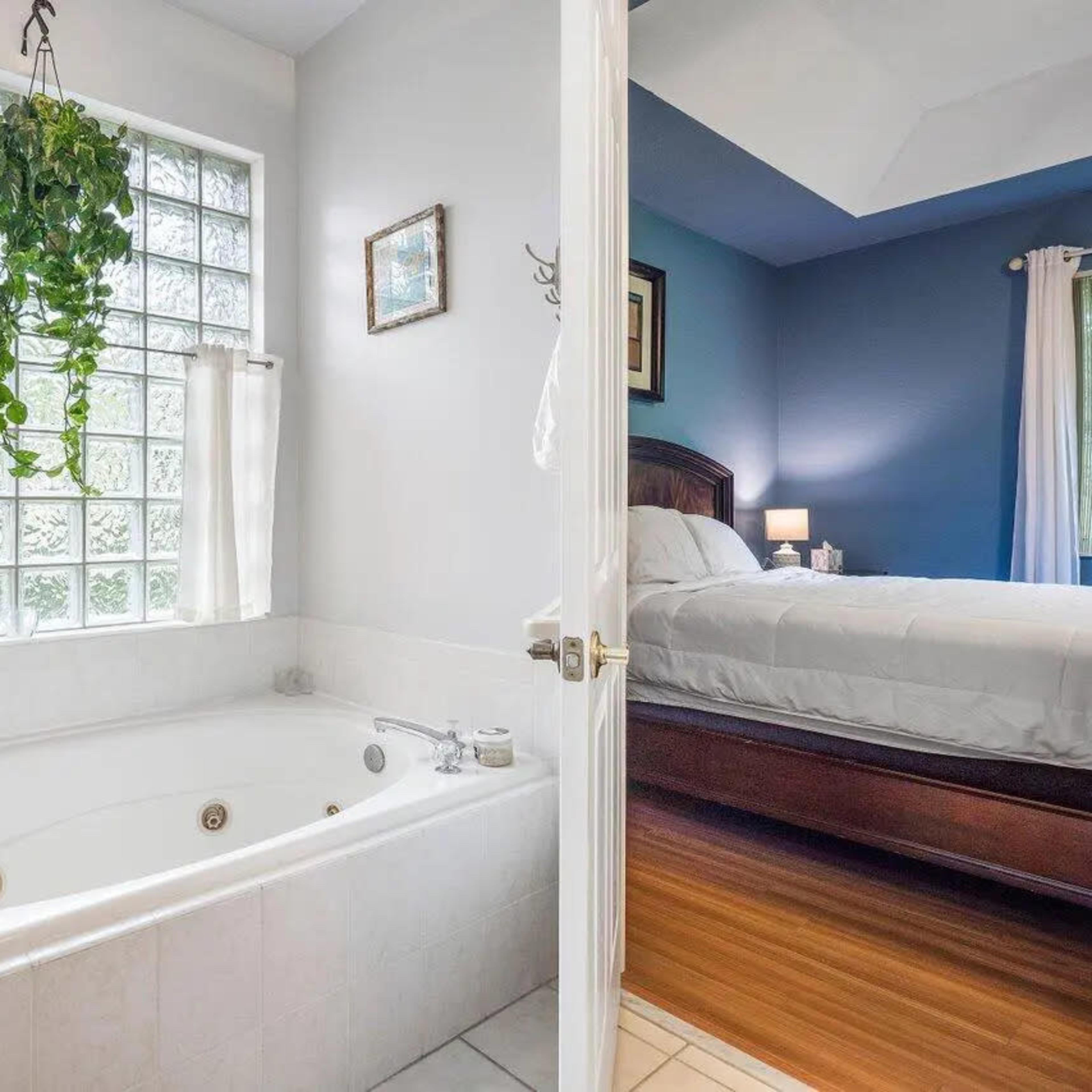 A bathroom featuring a large soaking tub next to a window with glass blocks, with a doorway leading into a bedroom.