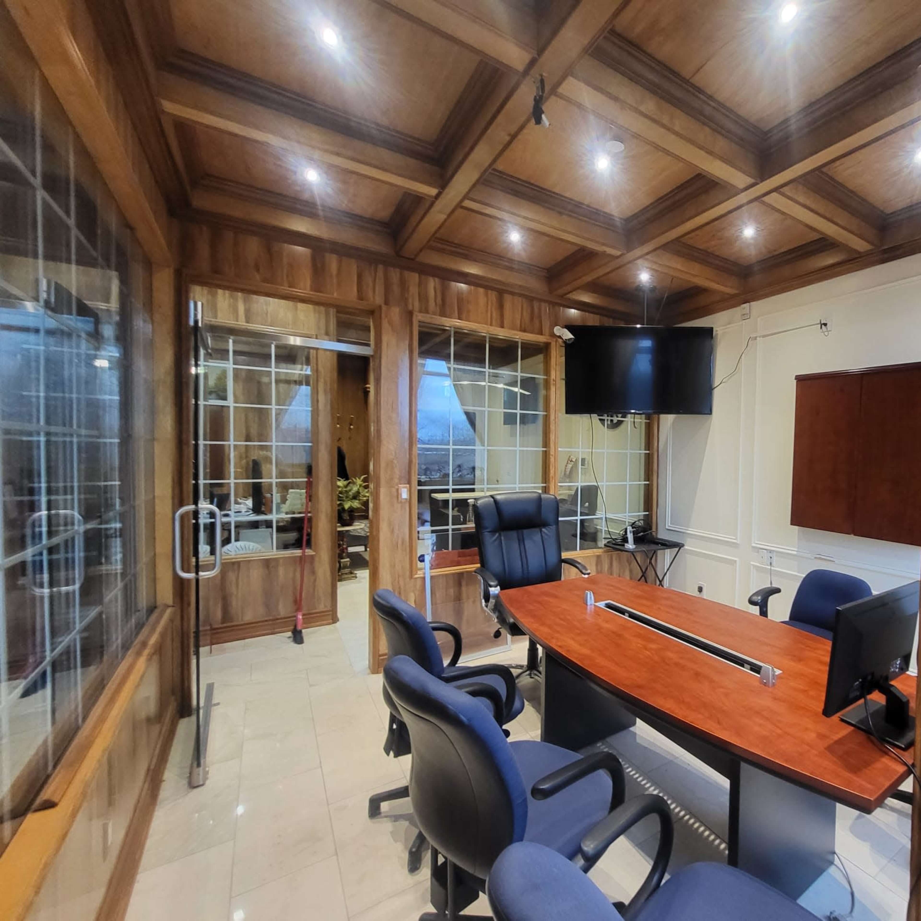 A well-designed office space featuring a wooden coffered ceiling, a large rectangular table, office chairs, and glass walls with a view to an outdoor area.