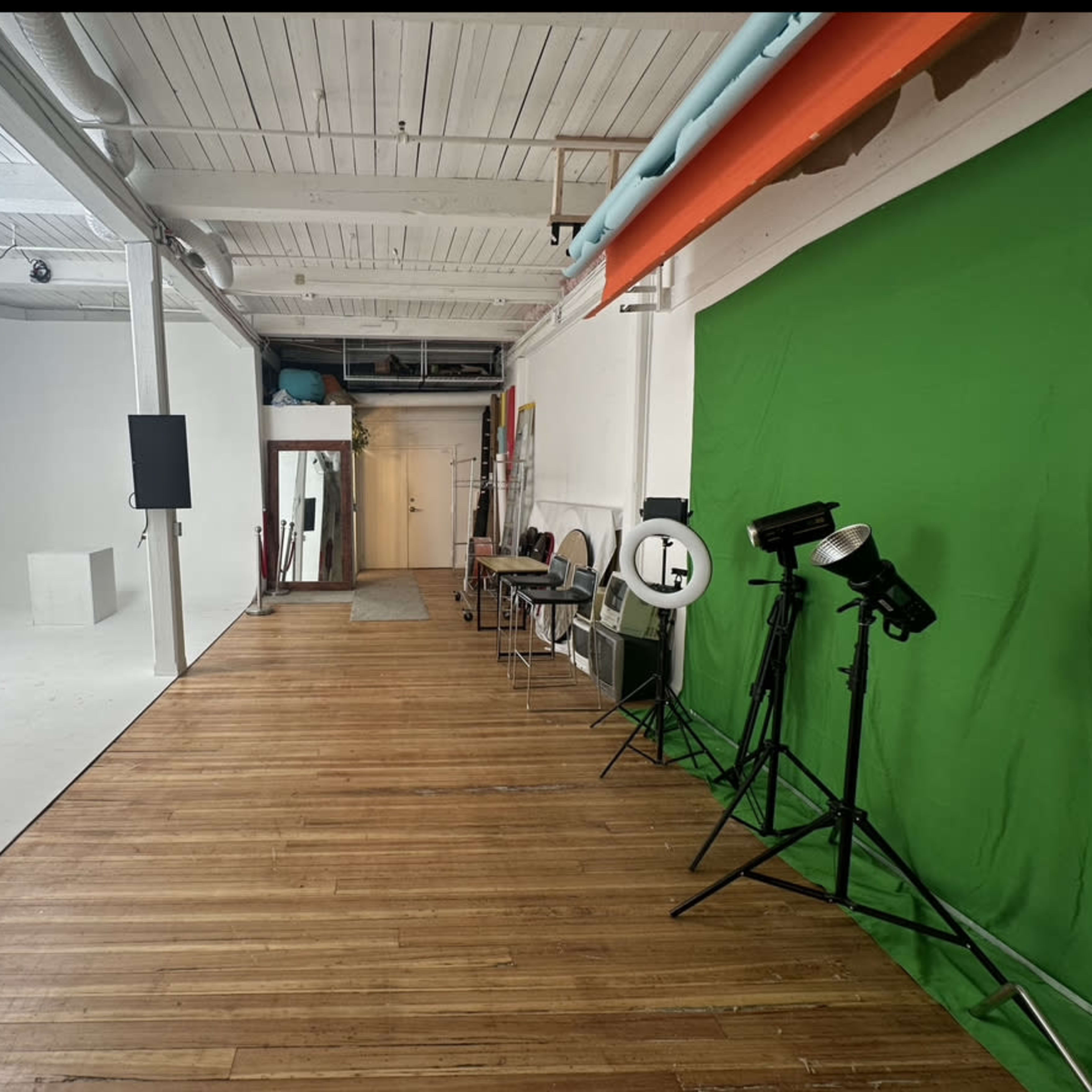 A spacious studio with a green screen, wooden flooring, and various lighting equipment on one side.