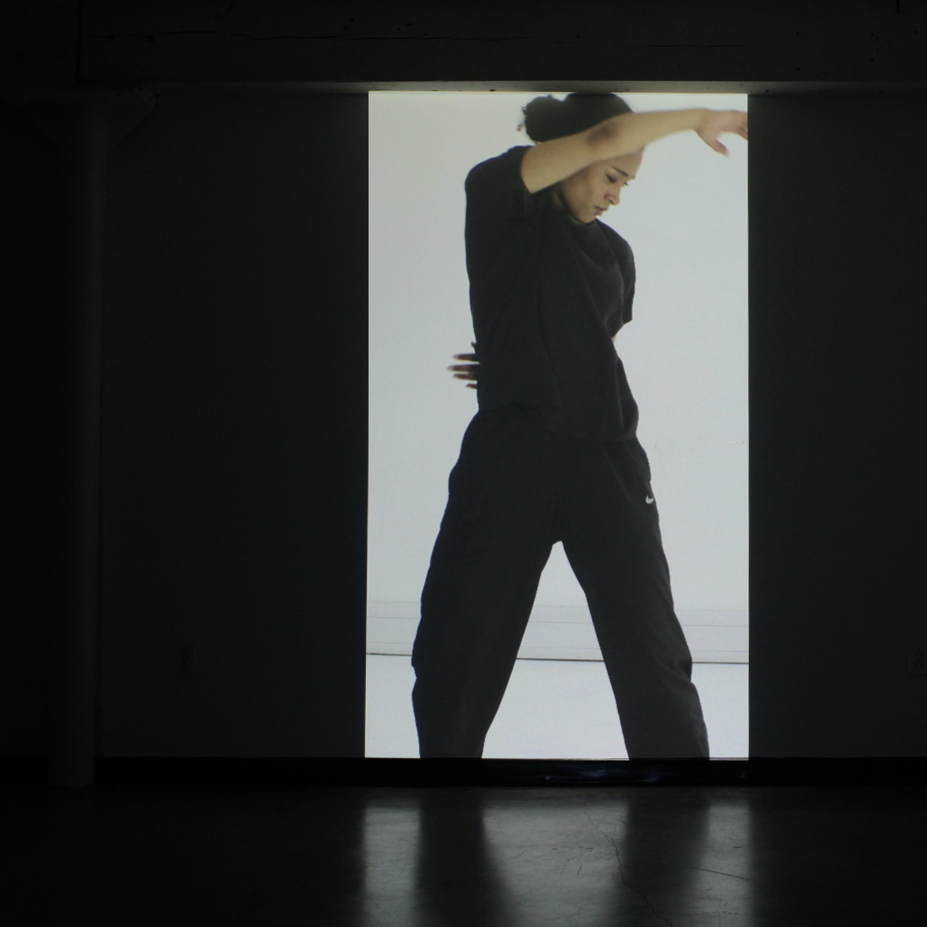 A dancer in a black outfit performs in front of a large, illuminated screen.
