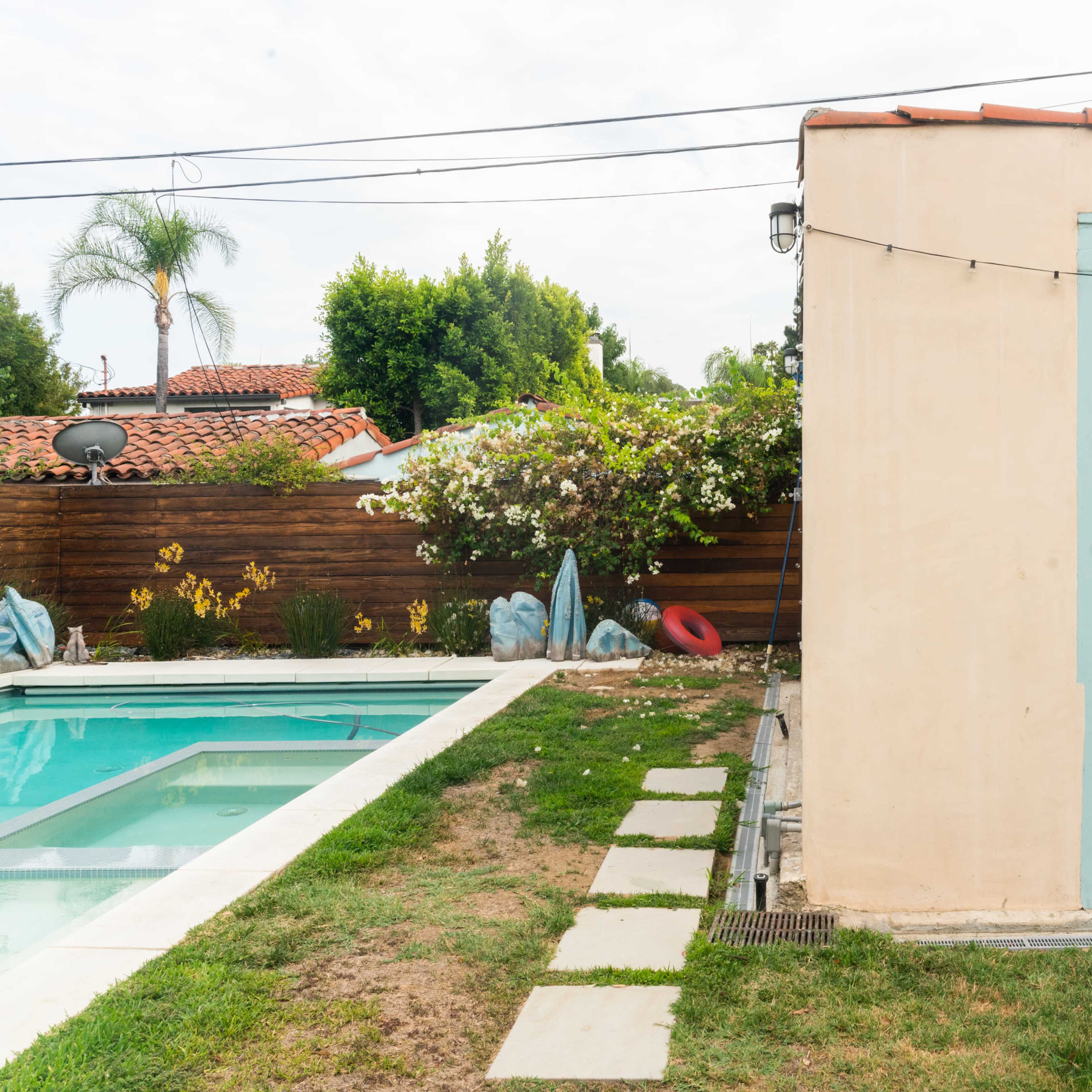 A backyard with a swimming pool, a light blue shed, and landscaped grass and plants.
