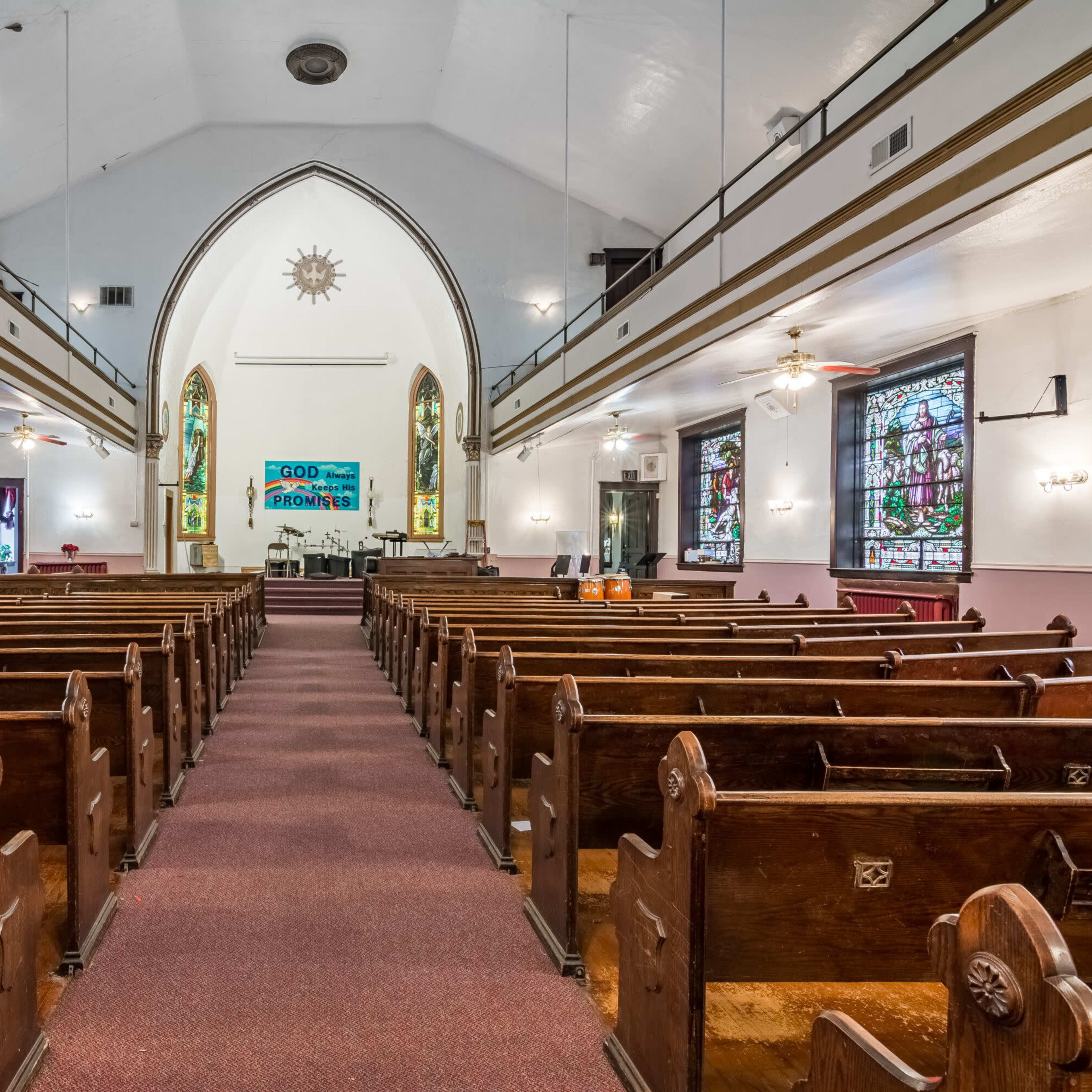 The interior of a church features wooden pews arranged in rows, with stained glass windows and a stage area at the front.