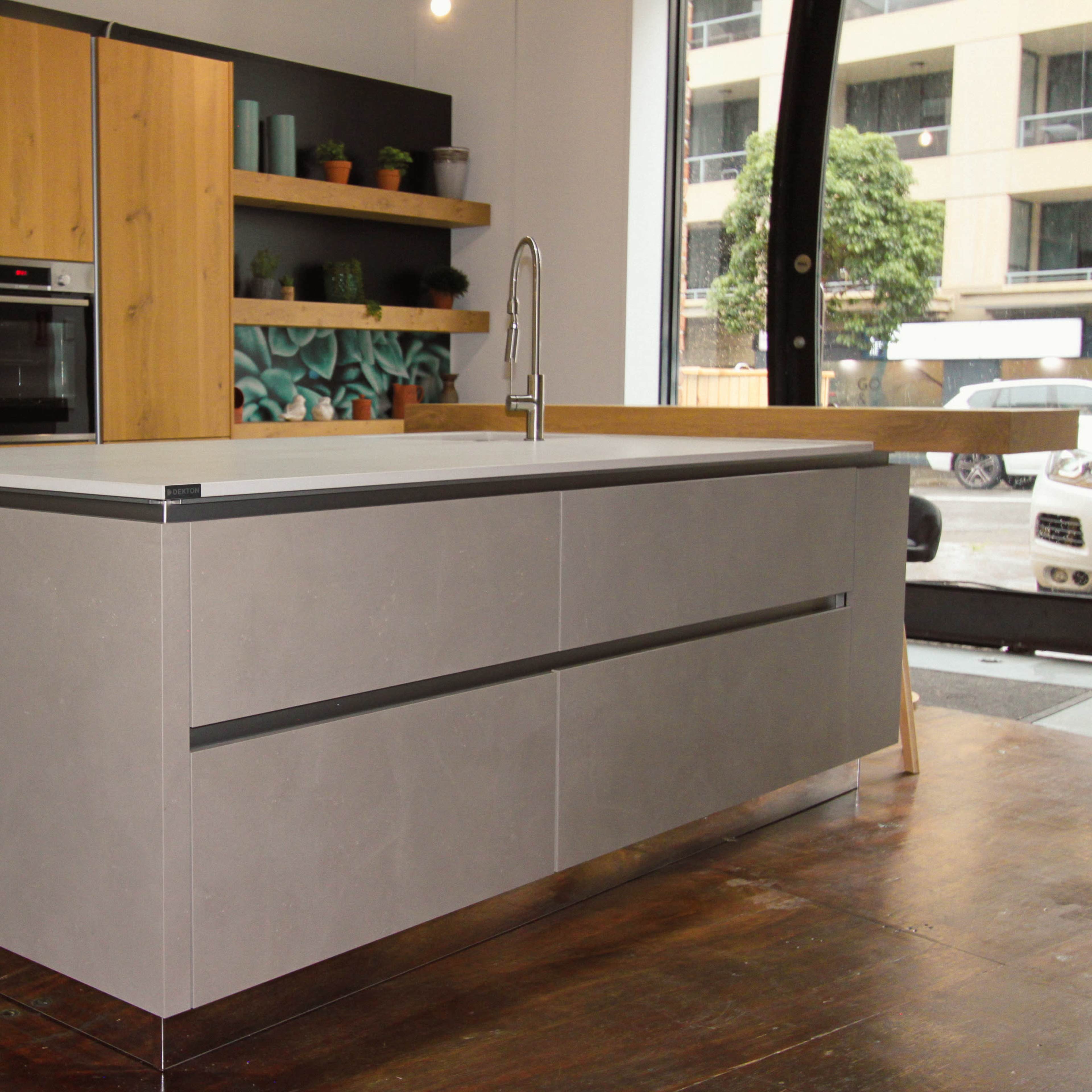 A modern kitchen with a central island, gray concrete countertops, and wooden cabinetry with open shelving displaying plants.