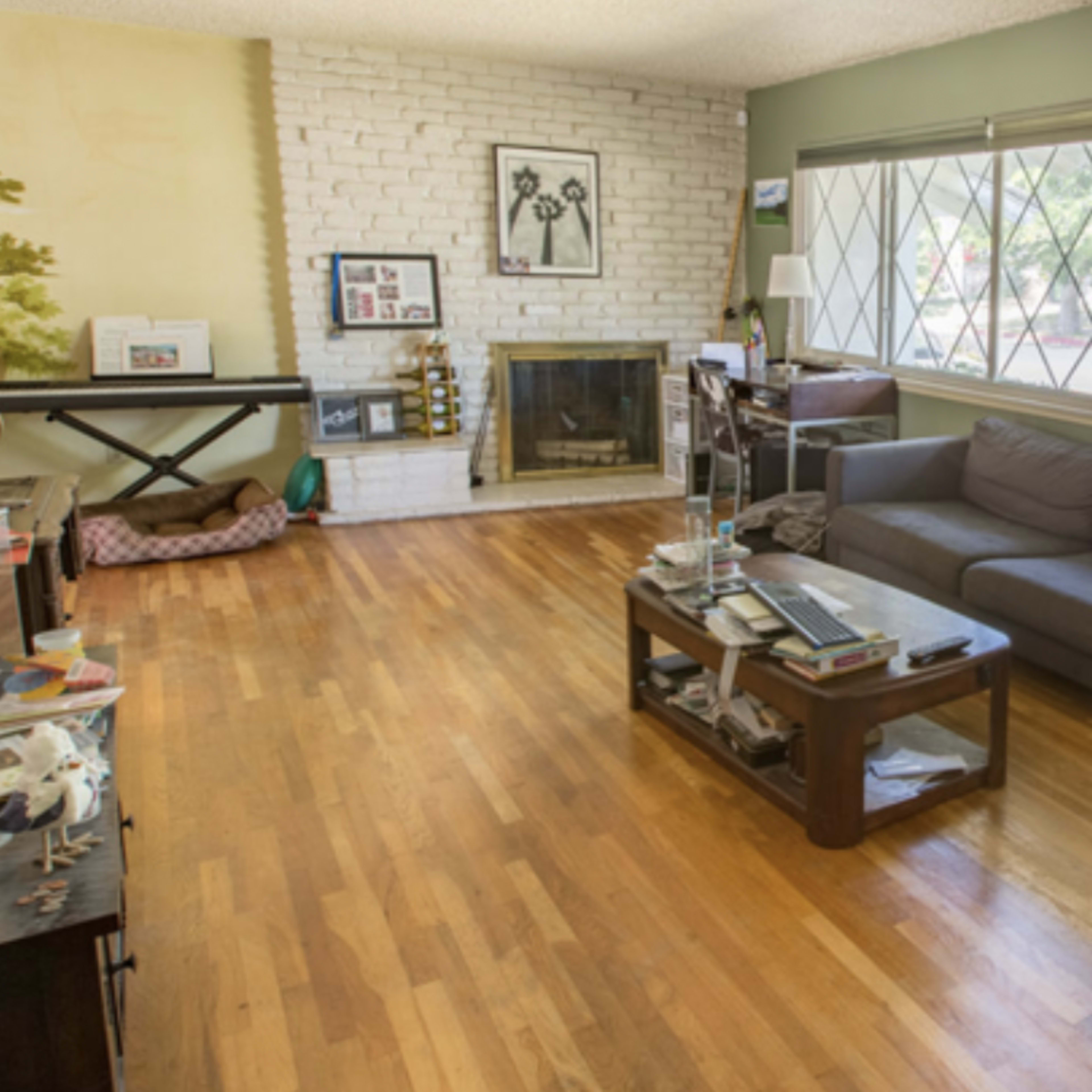 A living room with wooden flooring, a gray sofa, a fireplace, and a large window with diamond-patterned glass.