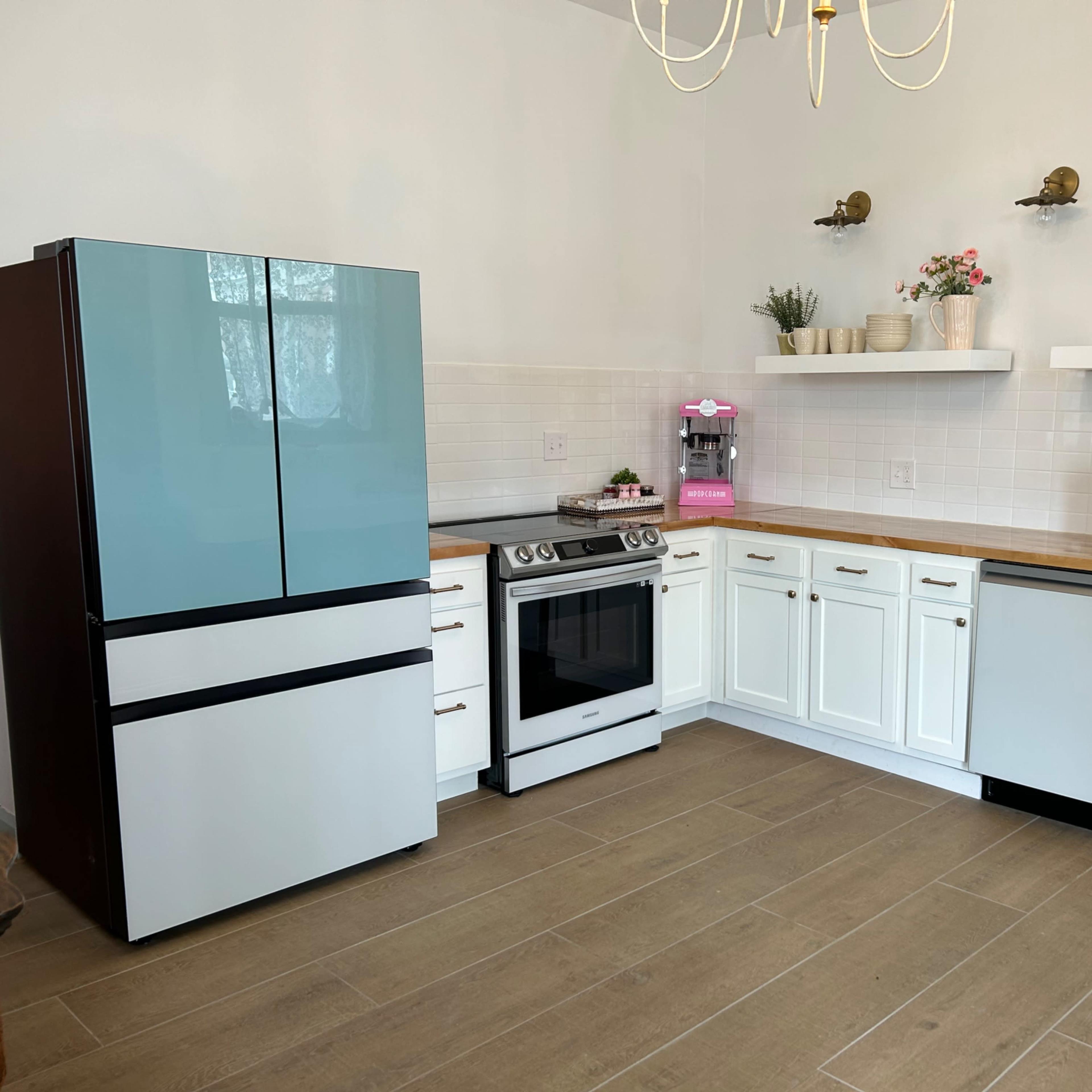 A modern kitchen with a blue and black refrigerator, stainless steel appliances, white cabinets, and wooden countertops.