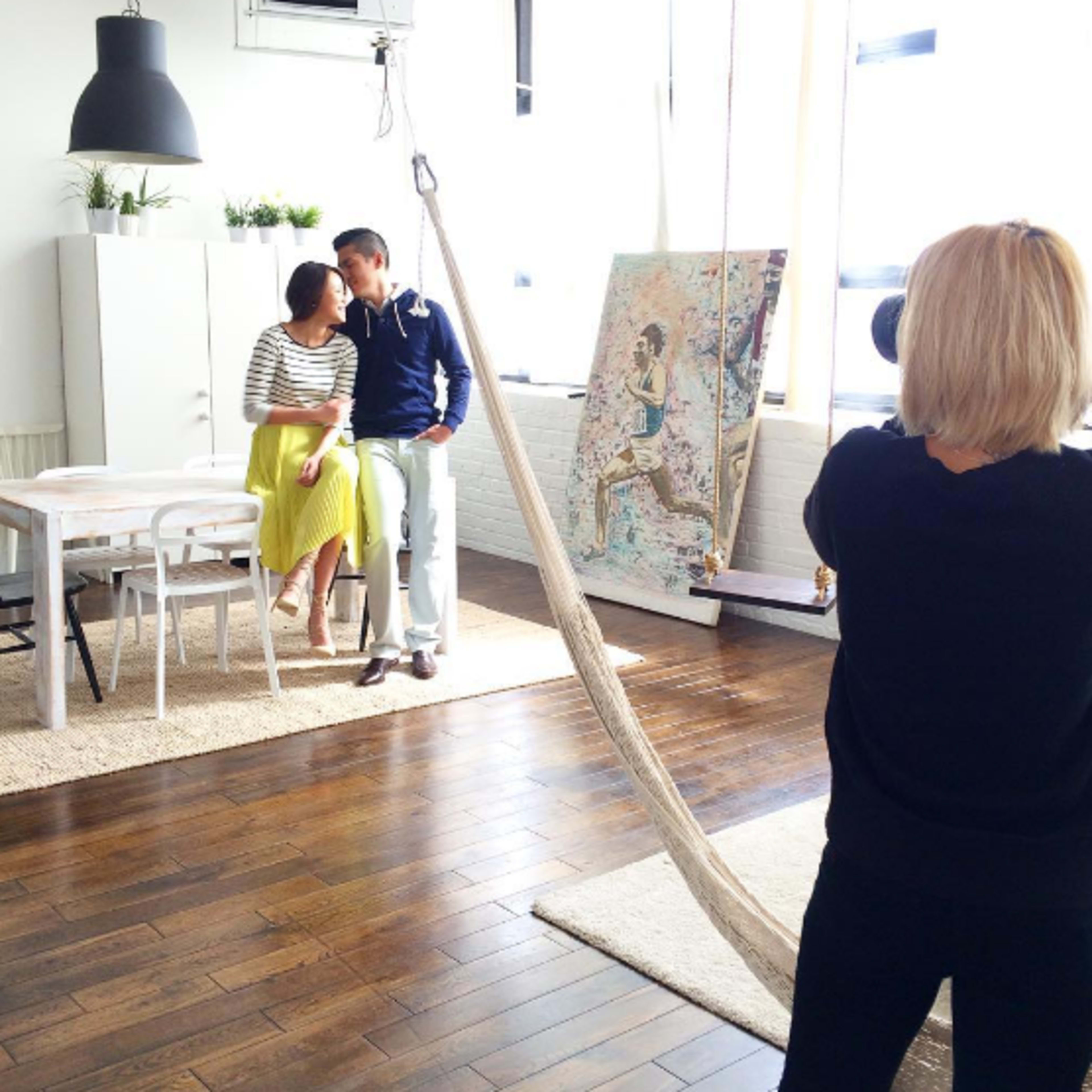 A photographer captures a couple posing in a brightly lit, modern room with wooden floors and contemporary decor.
