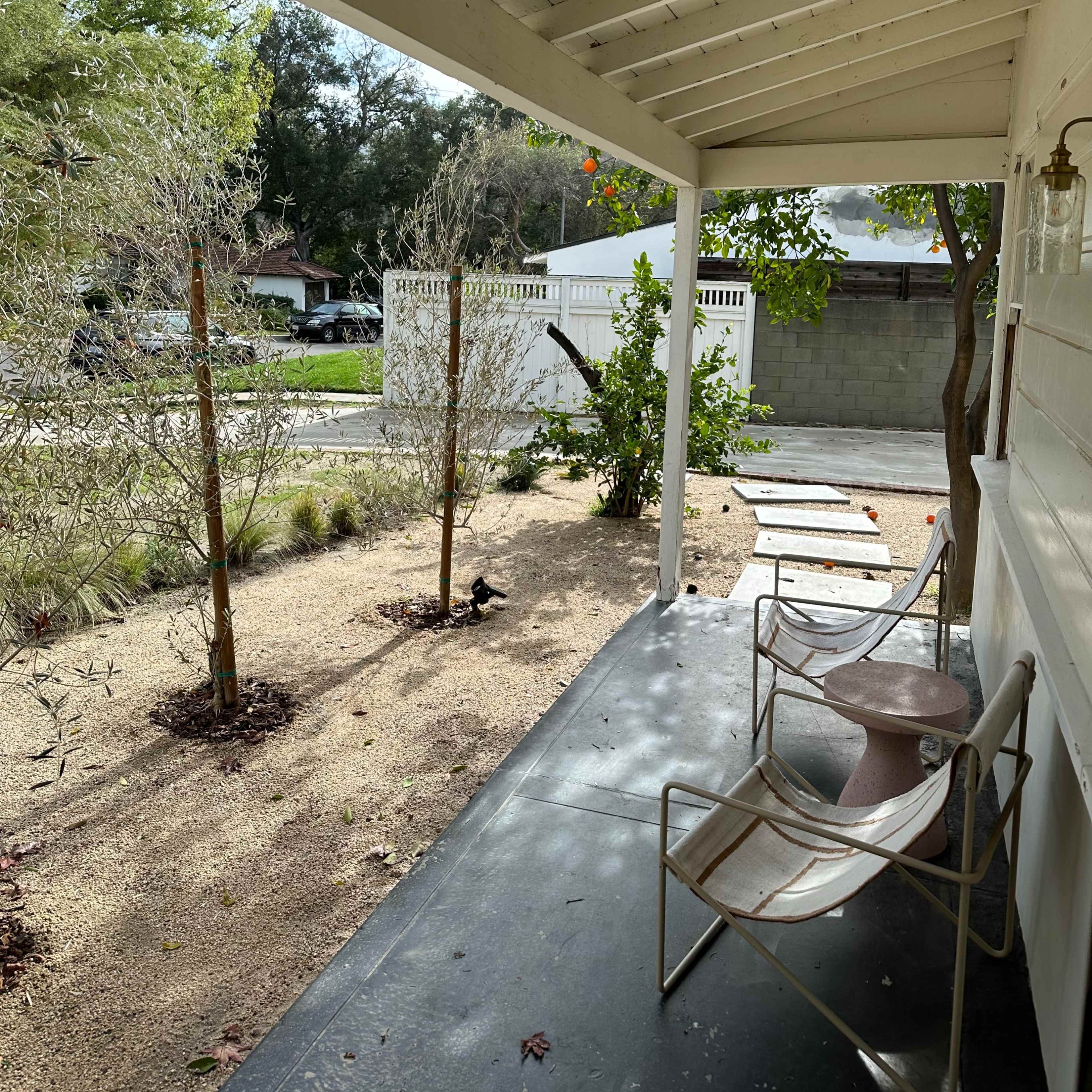 A porch with two metal chairs overlooks a landscaped front yard featuring small trees and gravel pathways.