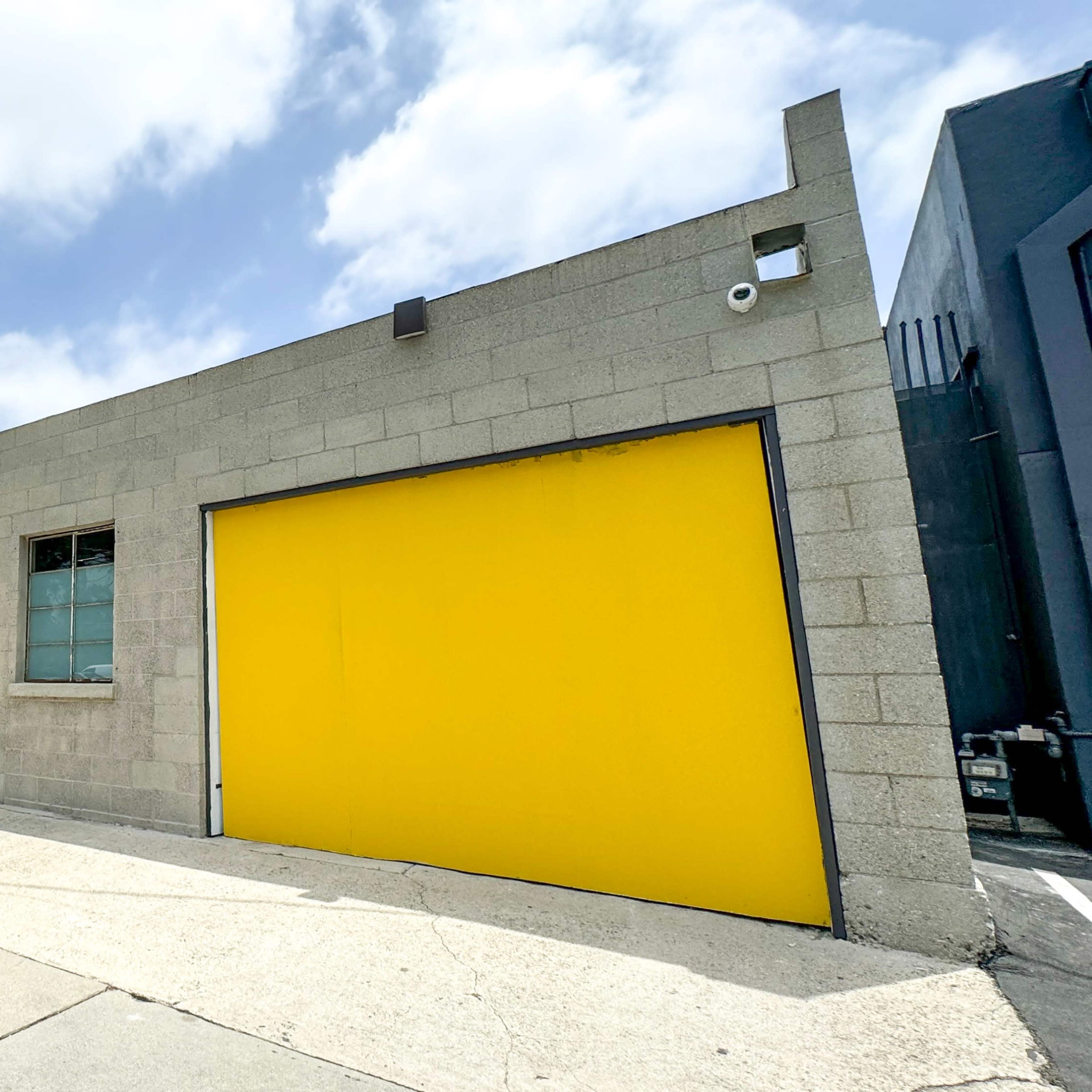 A gray building featuring a large yellow garage door and a matching entrance door, set along a sidewalk with power lines overhead.