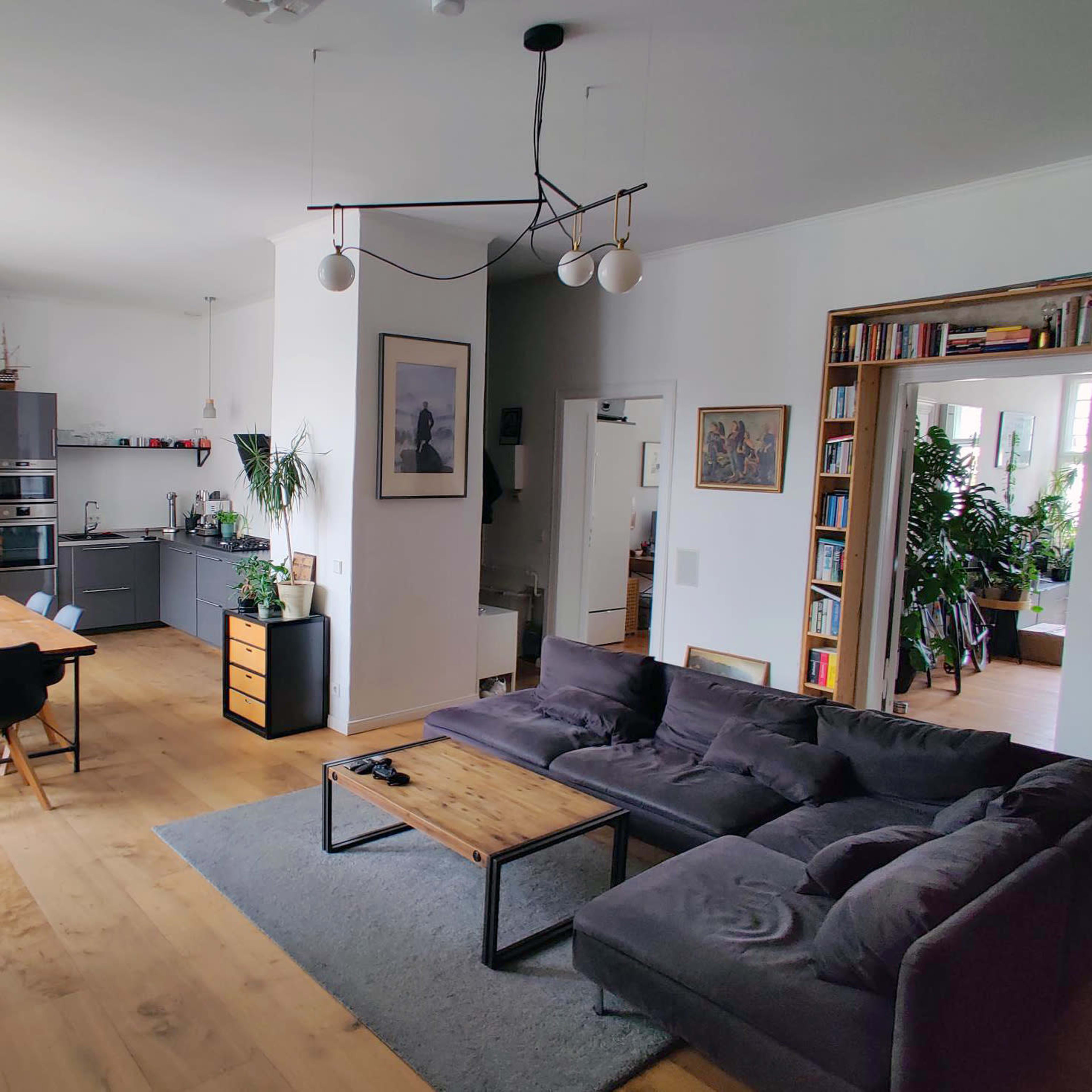 A spacious living area with a gray sectional sofa, a wooden coffee table, a dining table with chairs, and a modern kitchen in the background.
