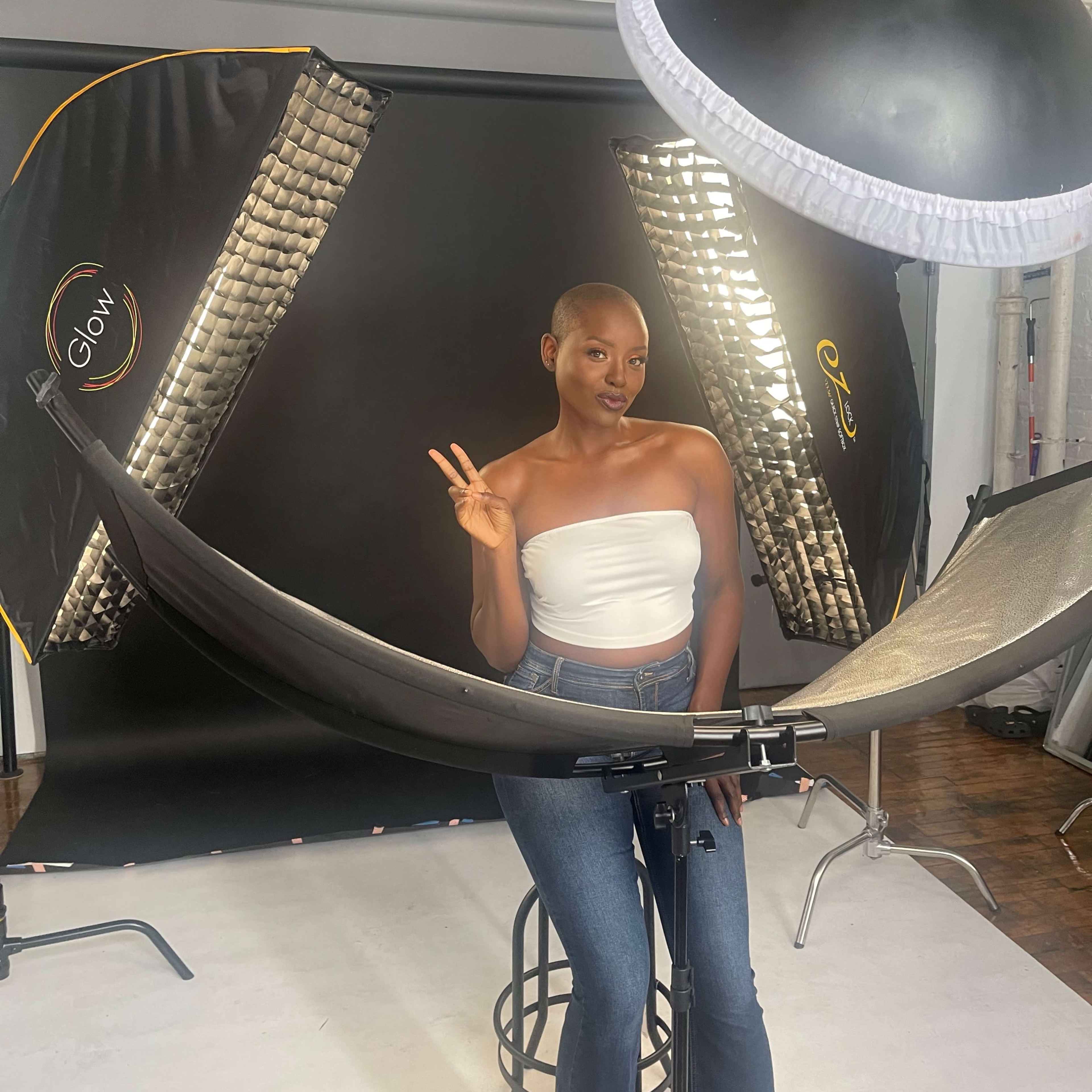 A person with a shaved head poses by a photography setup featuring softbox lights and a curved reflector.