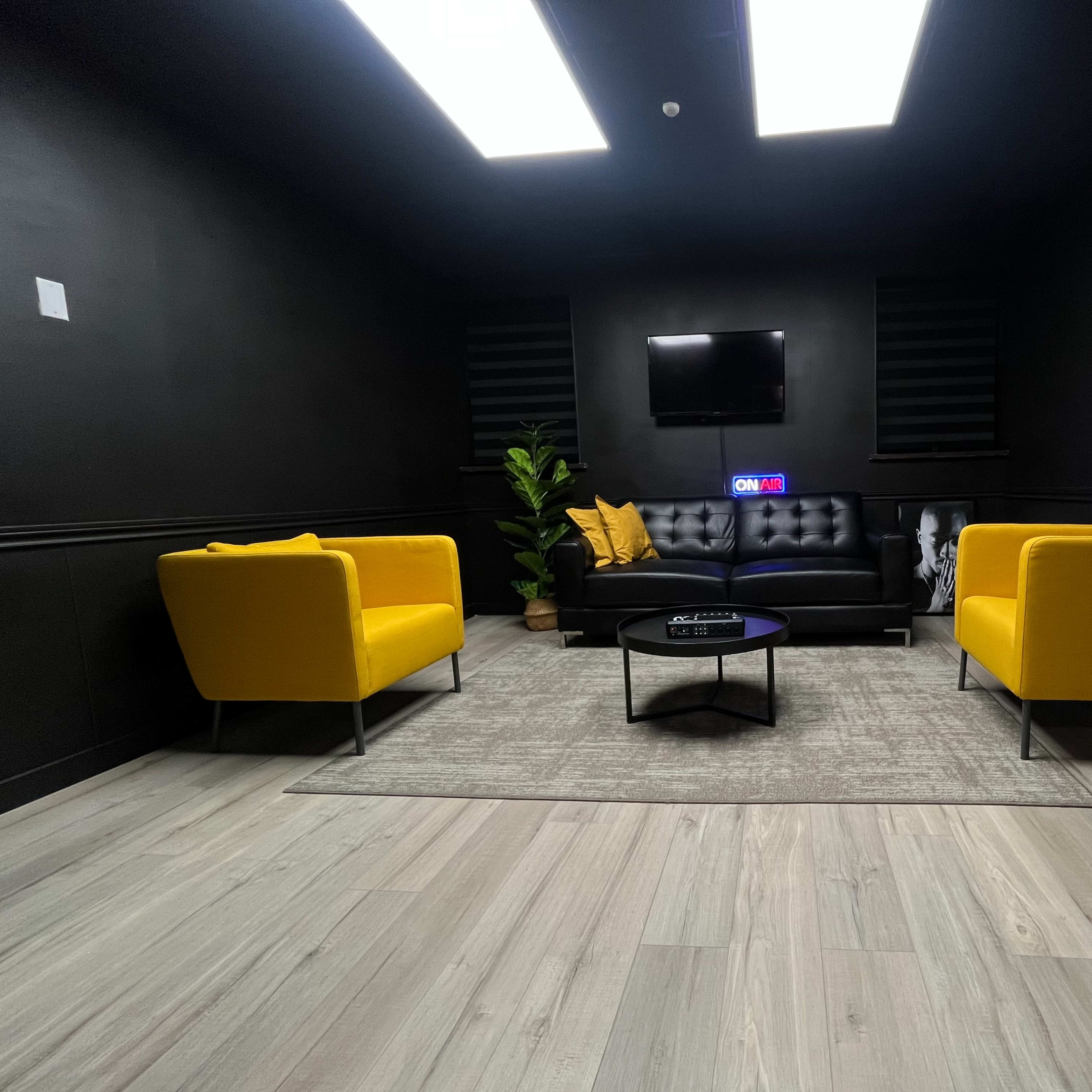 A modern lounge area with two yellow chairs, a black sofa, a small round table, and a plant against a dark backdrop.