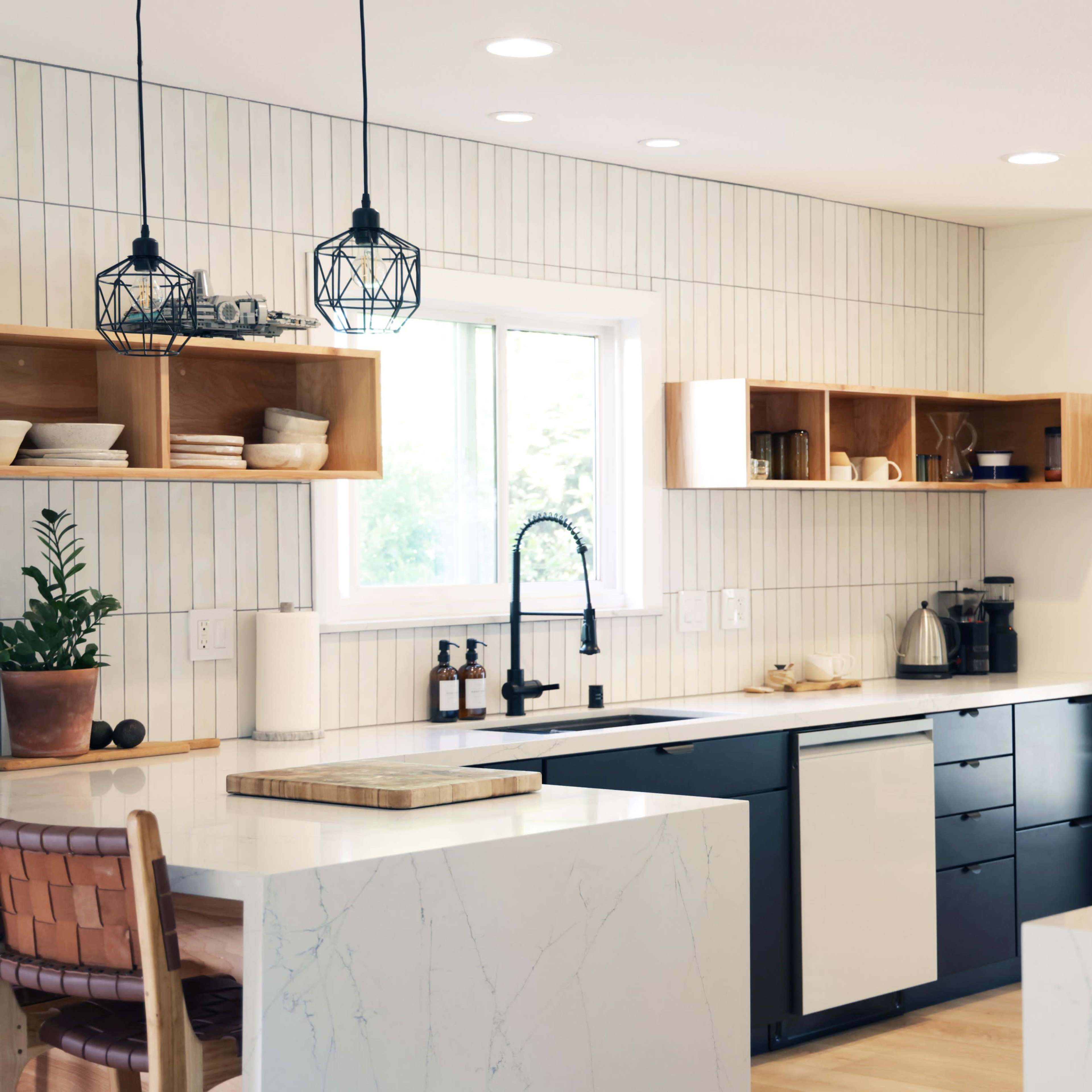The kitchen features modern black cabinets, a large island with a marble countertop, and wooden shelves against light-colored walls.