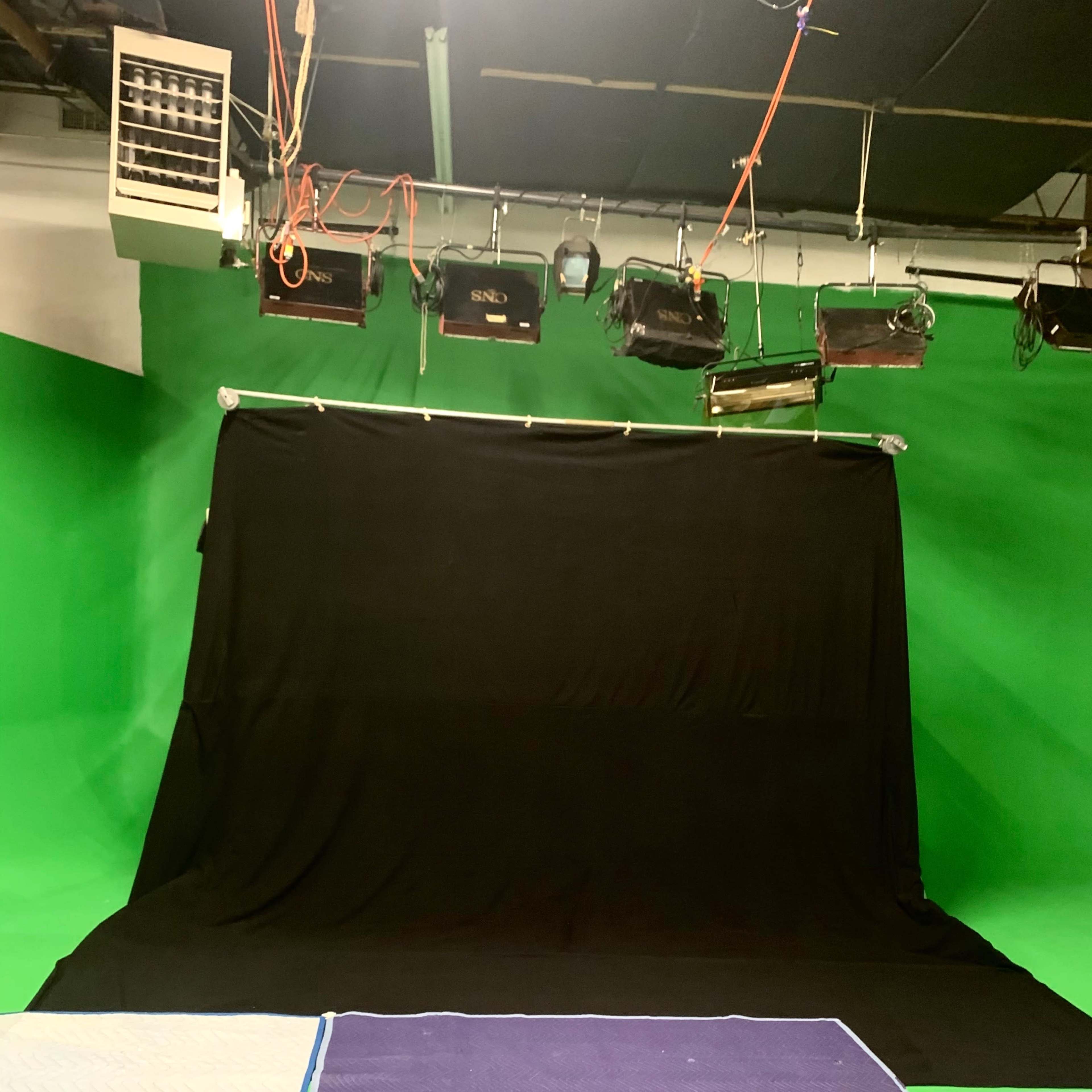 A studio setup with a black backdrop and green walls, along with several mats on the floor.