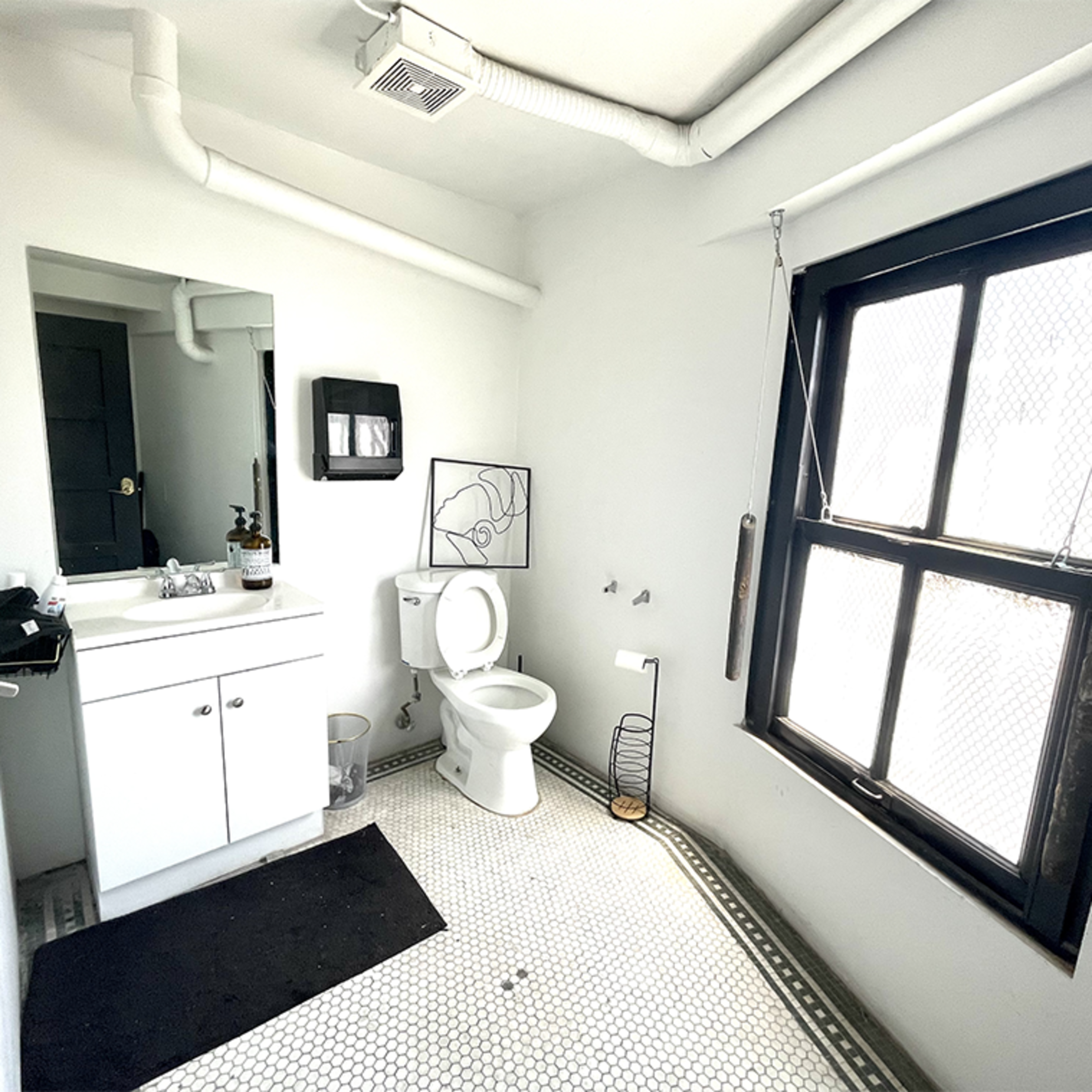 A simple, modern bathroom featuring a white vanity with a sink, a toilet, and a window with a black frame.