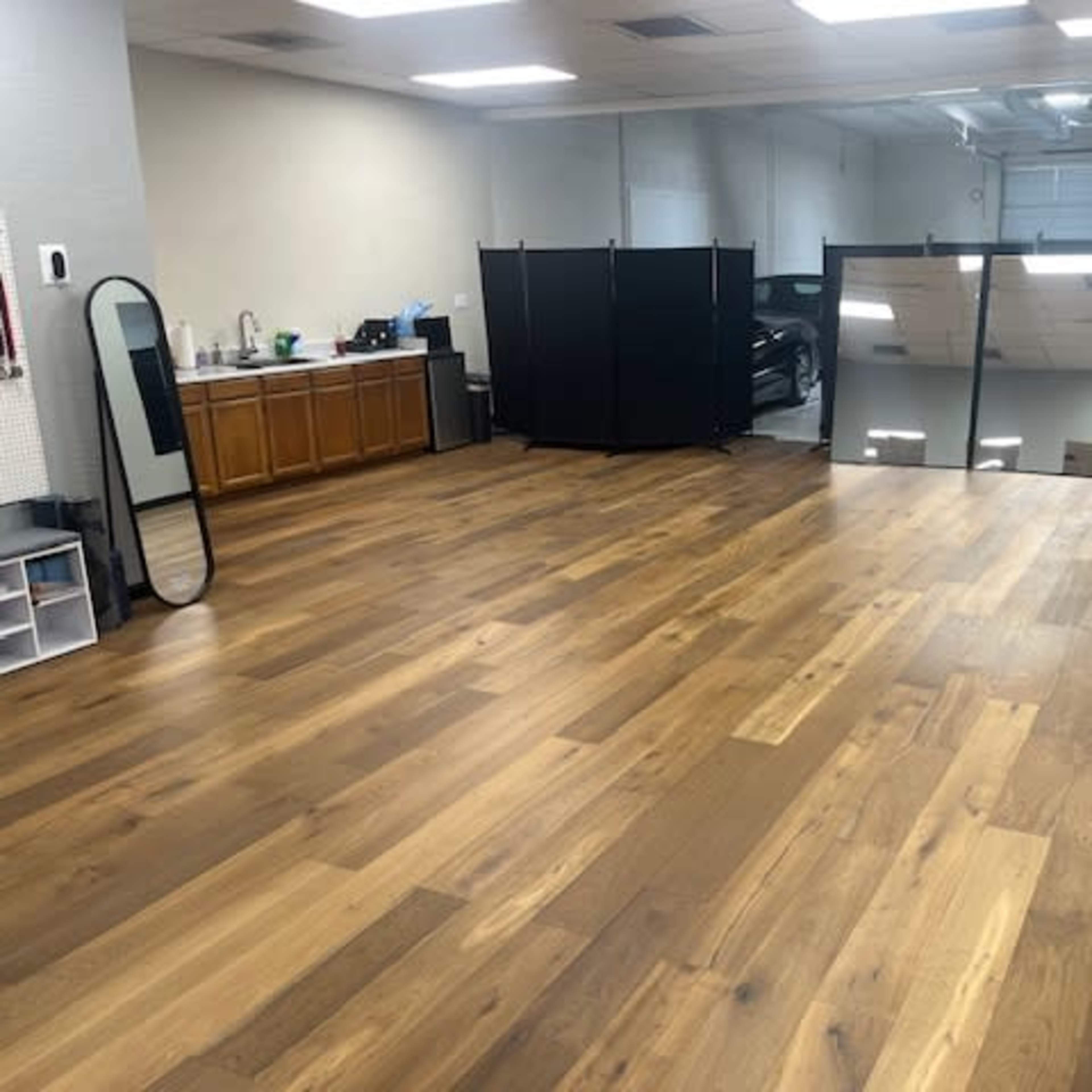 A spacious room with hardwood flooring, featuring a kitchen area and a mirrored wall, separated by a black partition.