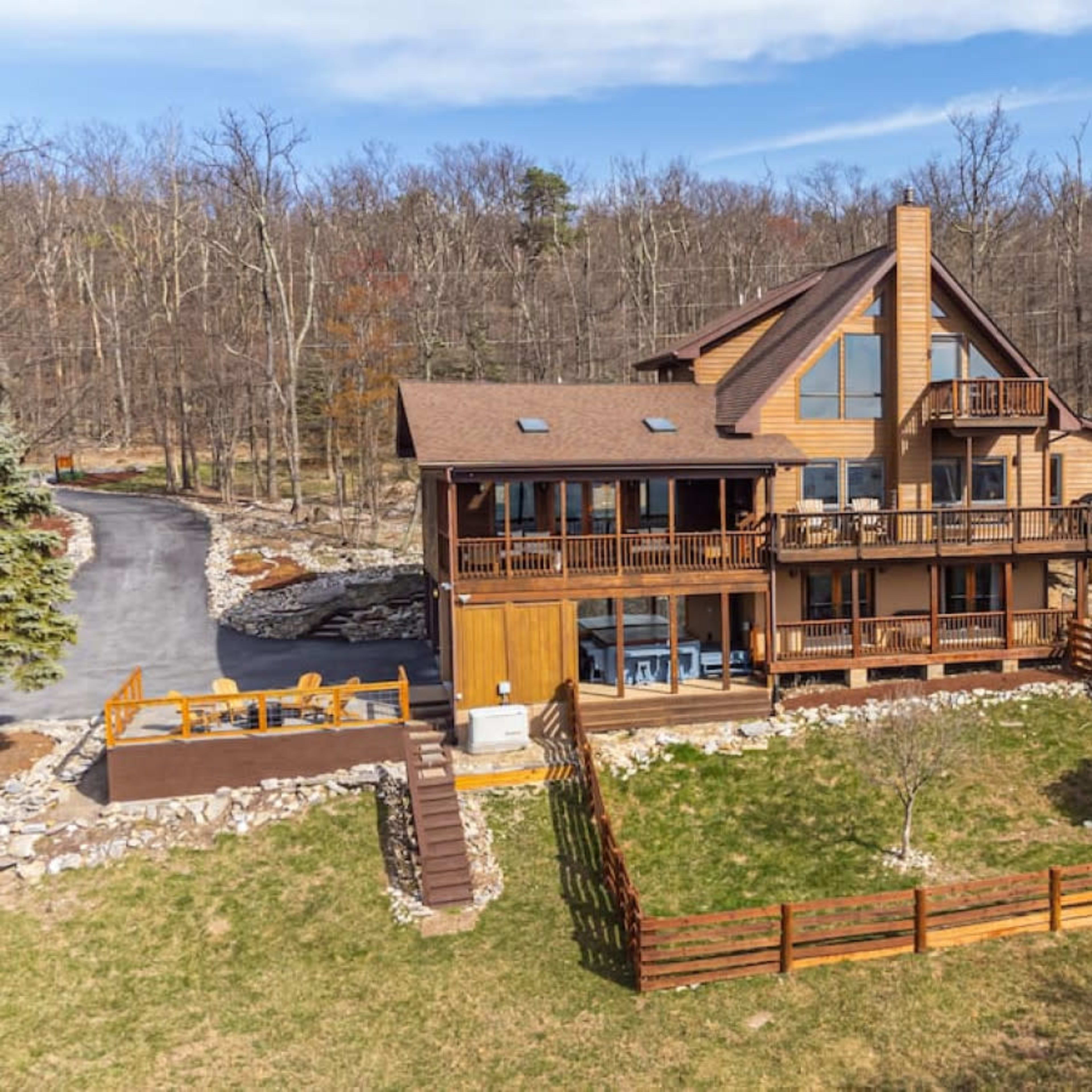 A large wooden house with multiple balconies and a deck overlooks a grassy yard surrounded by trees.