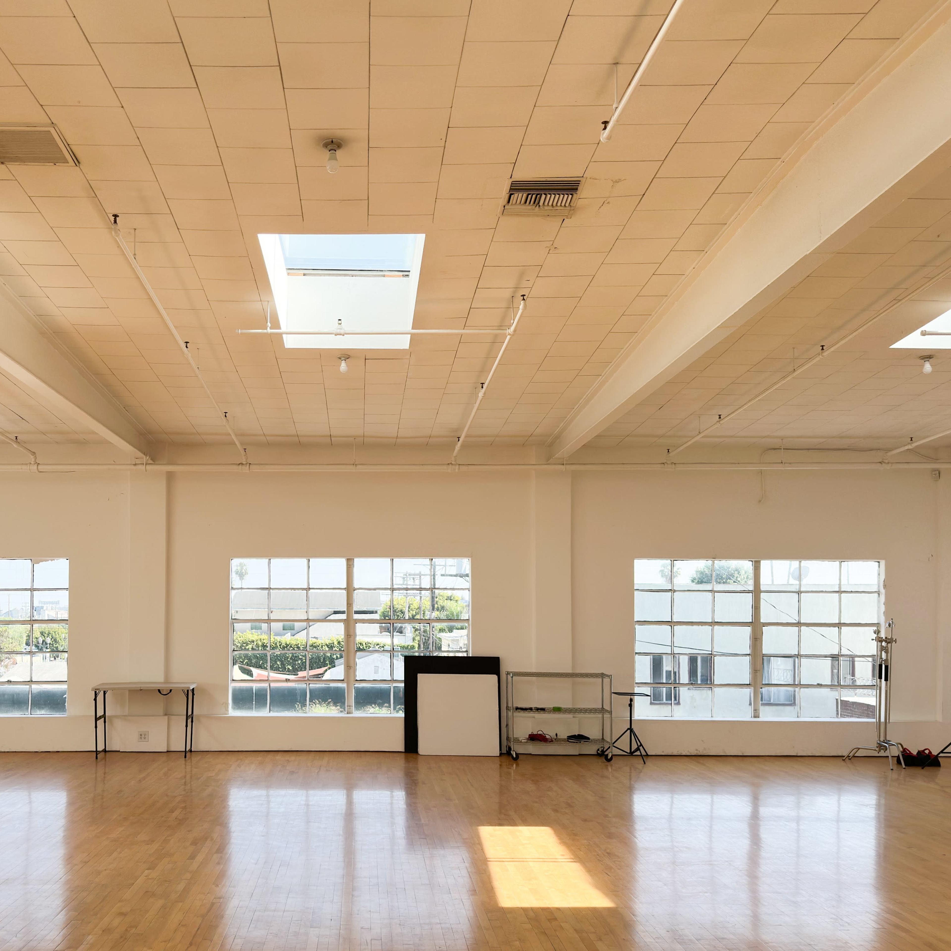 A spacious, vacant room with large windows and wooden flooring is illuminated by natural light from skylights above.