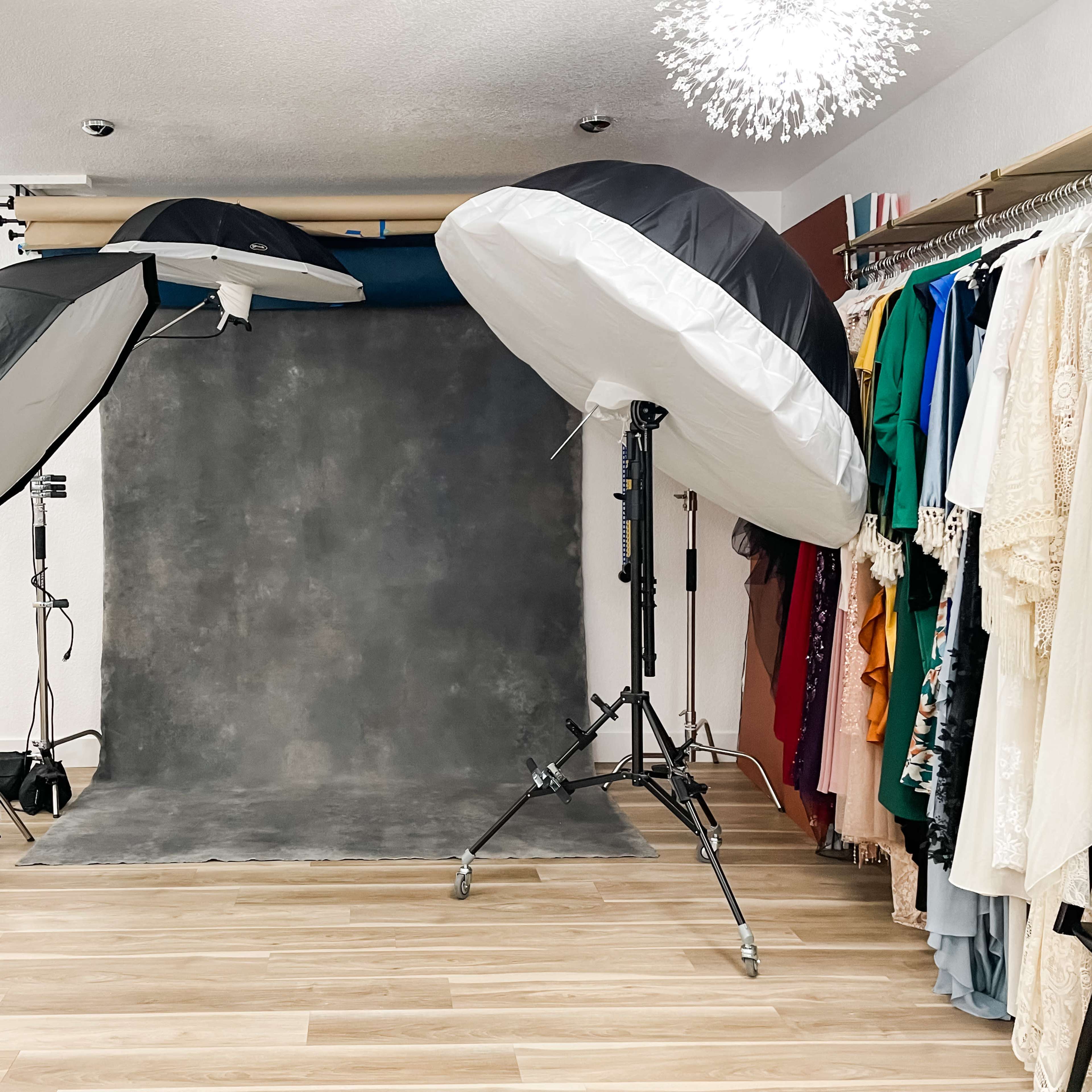 A photography studio set up with large softbox lights aiming at a gray backdrop, alongside a rack of colorful clothing.