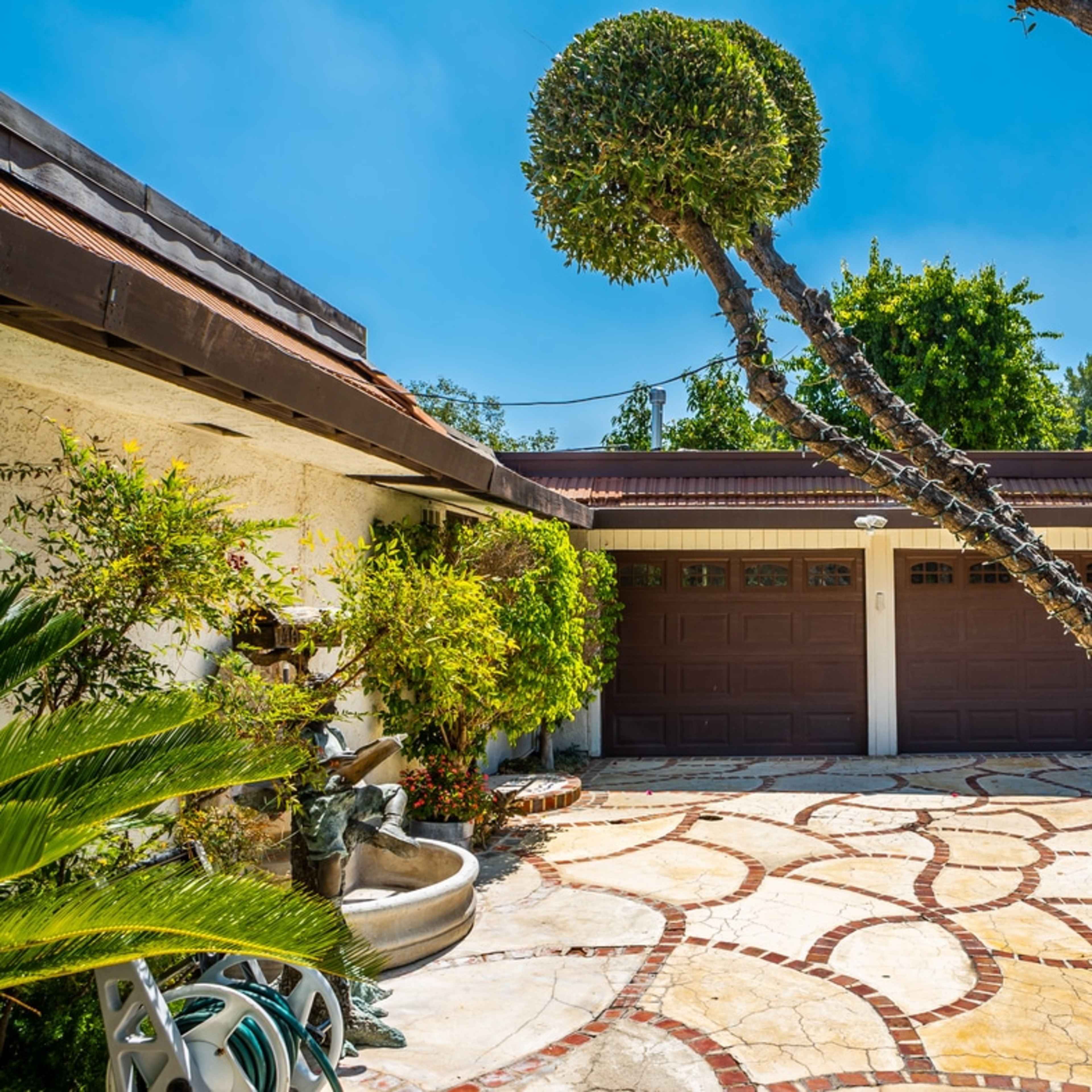 A house with a patterned stone driveway, a fountain at the side, and a garage with brown doors.