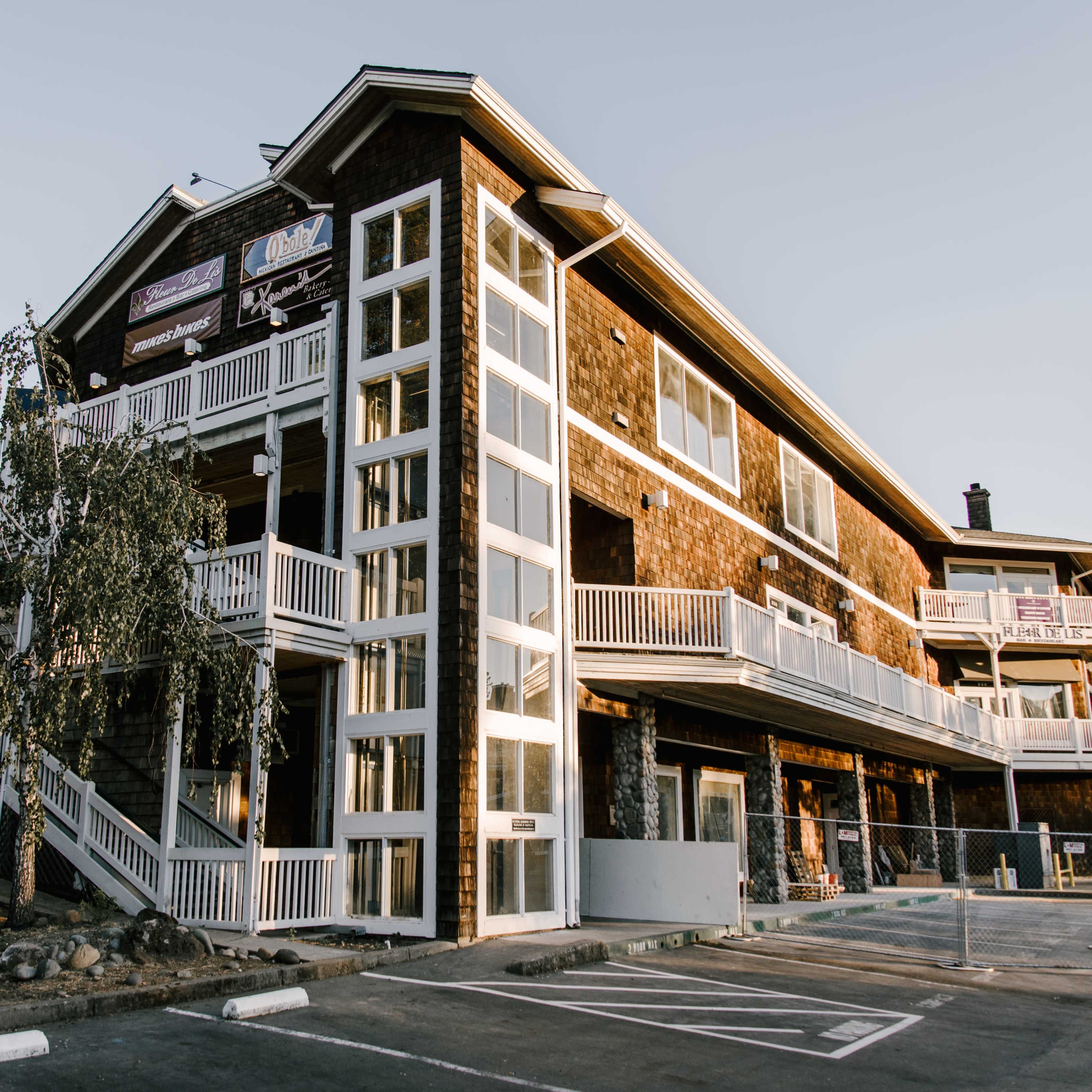 A three-story wooden building with multiple balconies and large windows is located on a sloped lot.