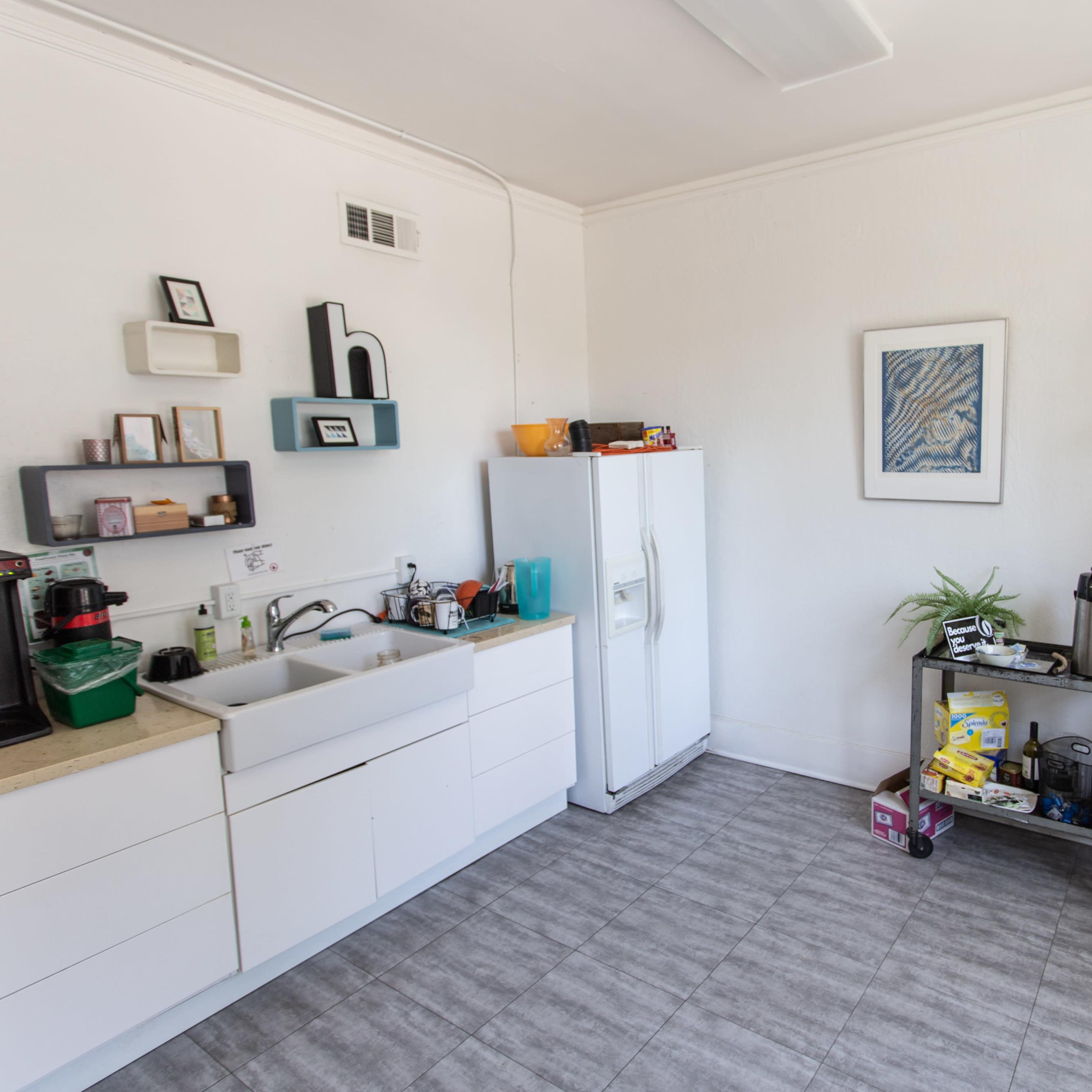 The kitchen features a white refrigerator, a farmhouse sink, and a shelving unit displaying various dishes and glassware.