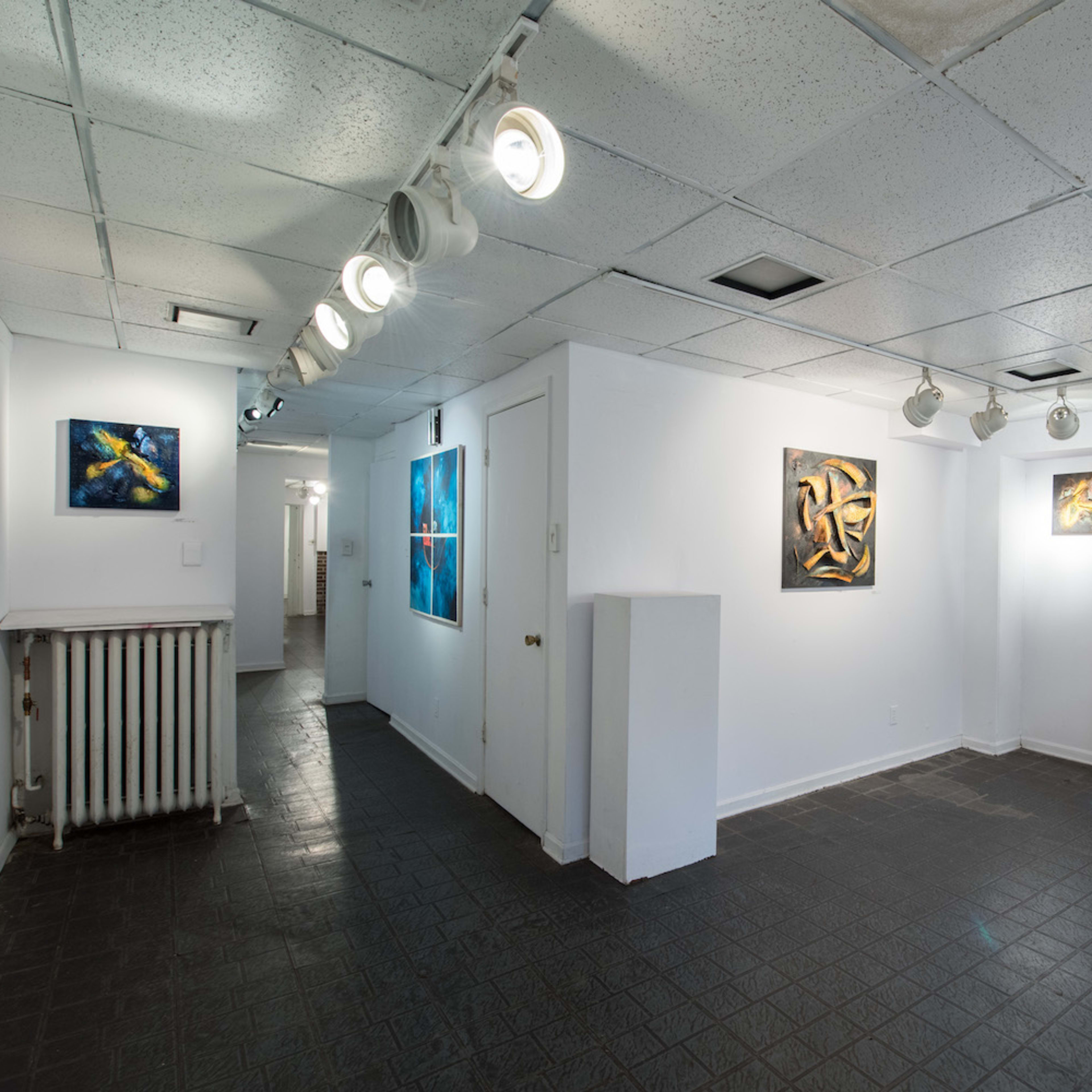 A spacious art gallery featuring several abstract paintings on white walls and a dark tiled floor.