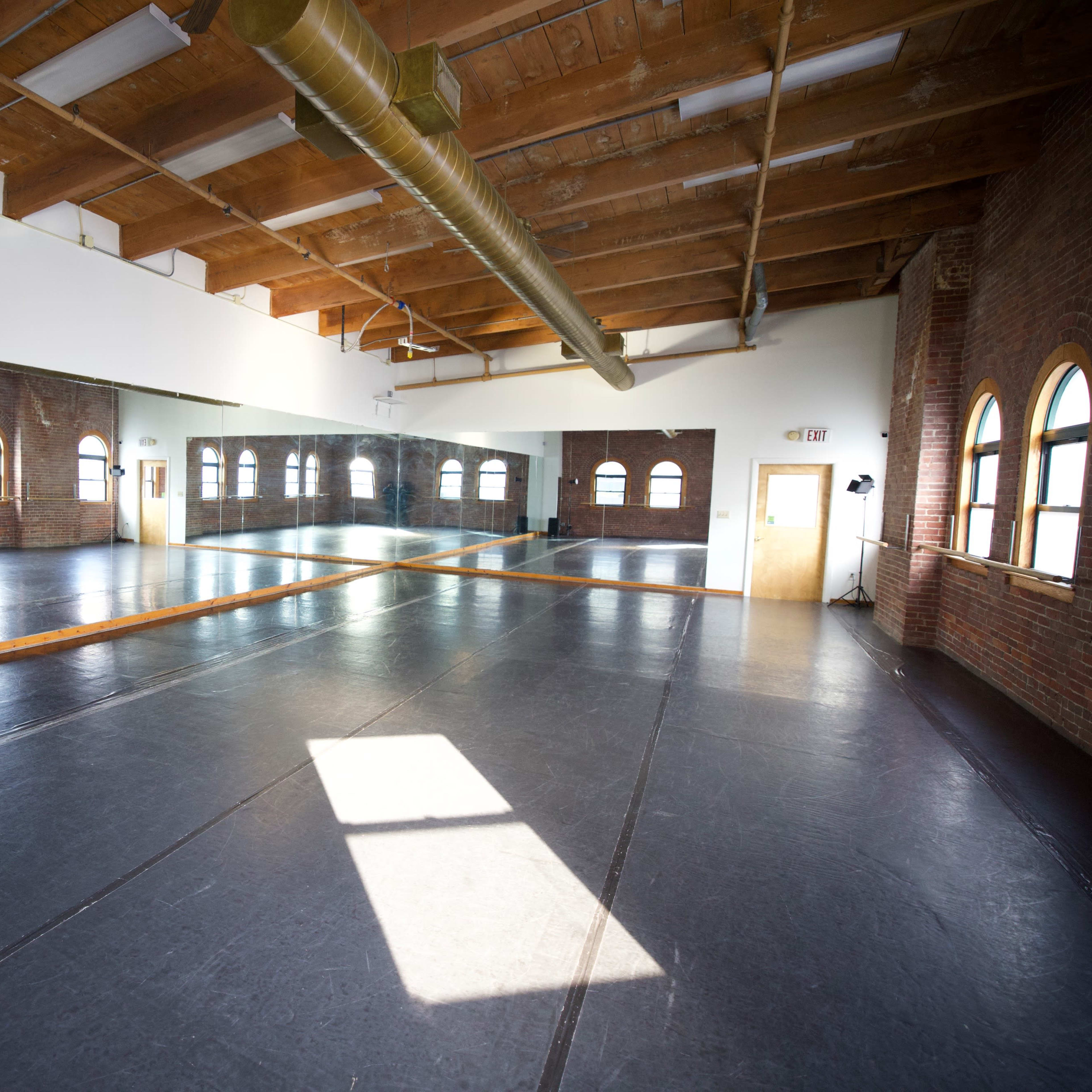 A spacious dance studio with wooden beams, large windows, and a mirrored wall.