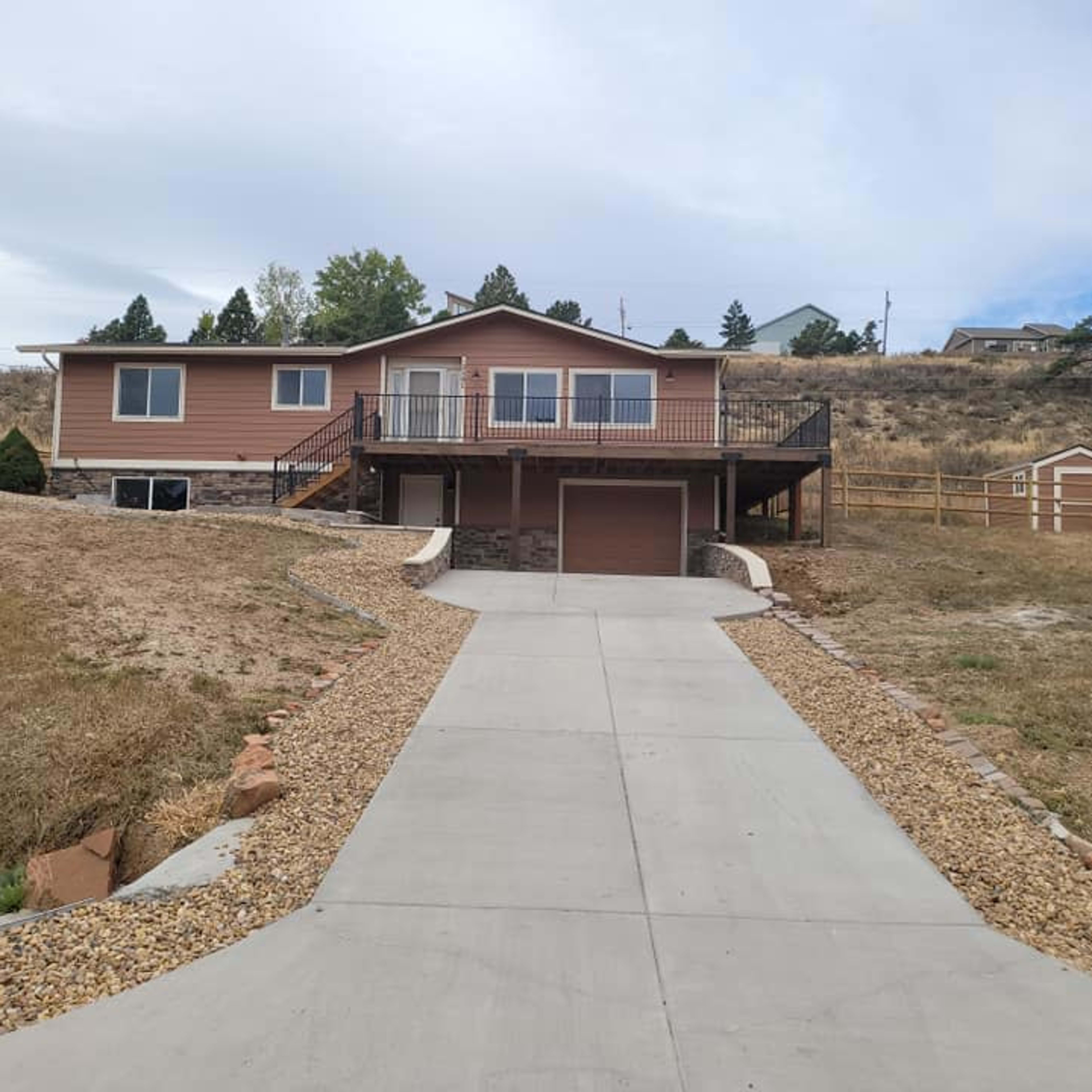 A single-story house with a driveway leading up to it, surrounded by dry grass and a few trees in the background.