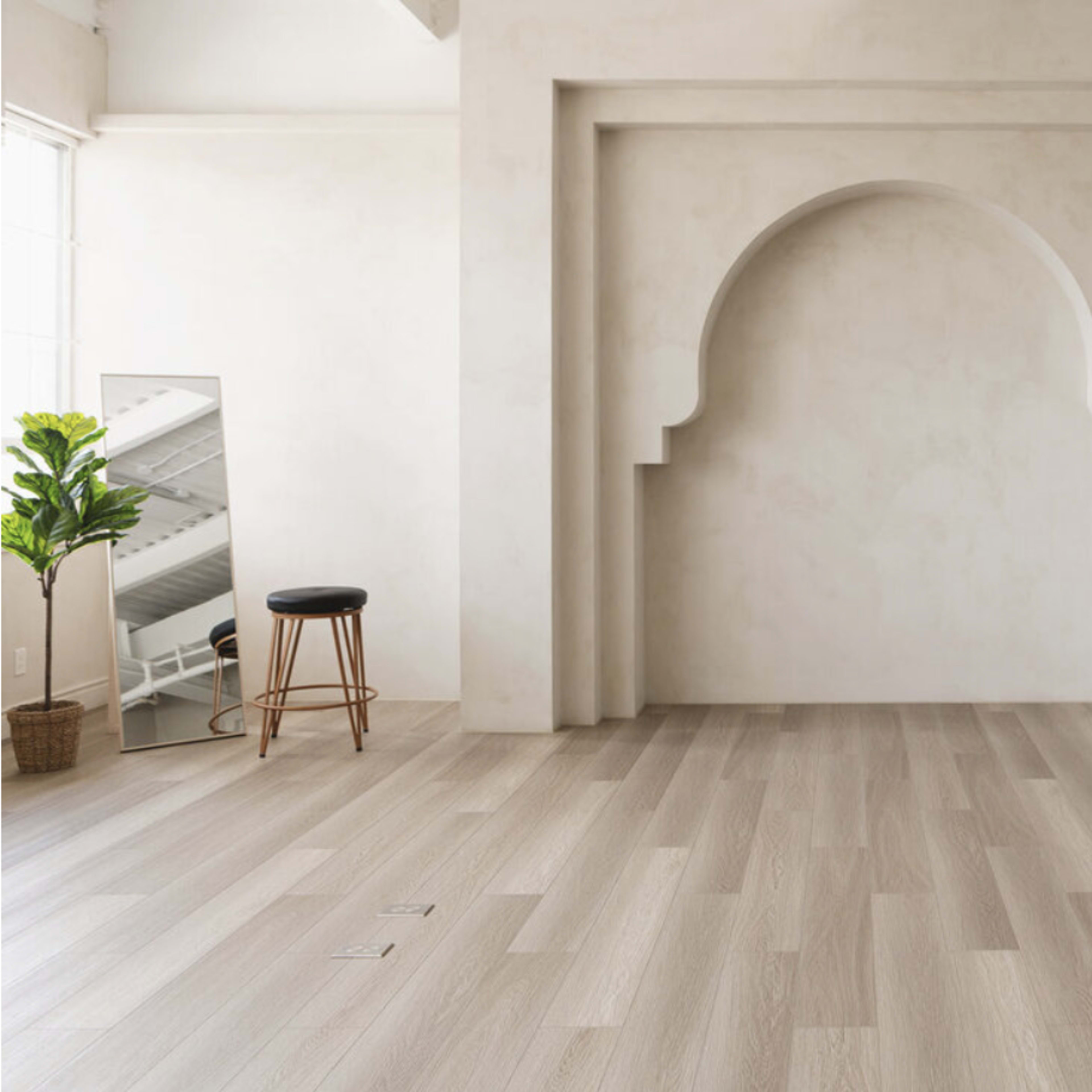 A spacious room with light-colored wood flooring, a large arched wall recess, a stool, a mirror, and a potted plant.